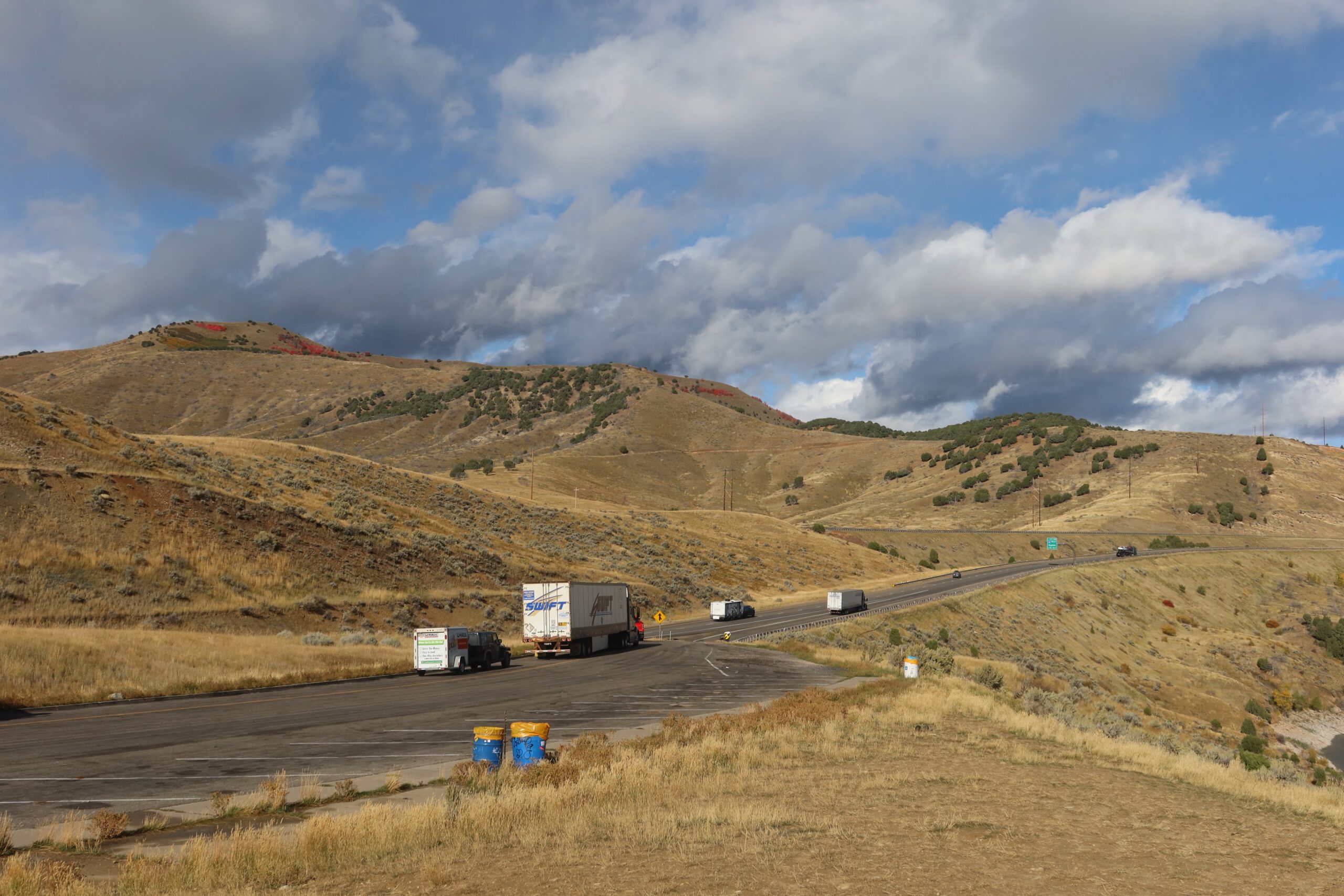 Roadside parking lot along Interstate 80 near Echo Reservoir in Coalville Utah, with trucks stopping at a scenic viewpoint overlooking rolling hills and dramatic cloud formations during a Utah road trip.