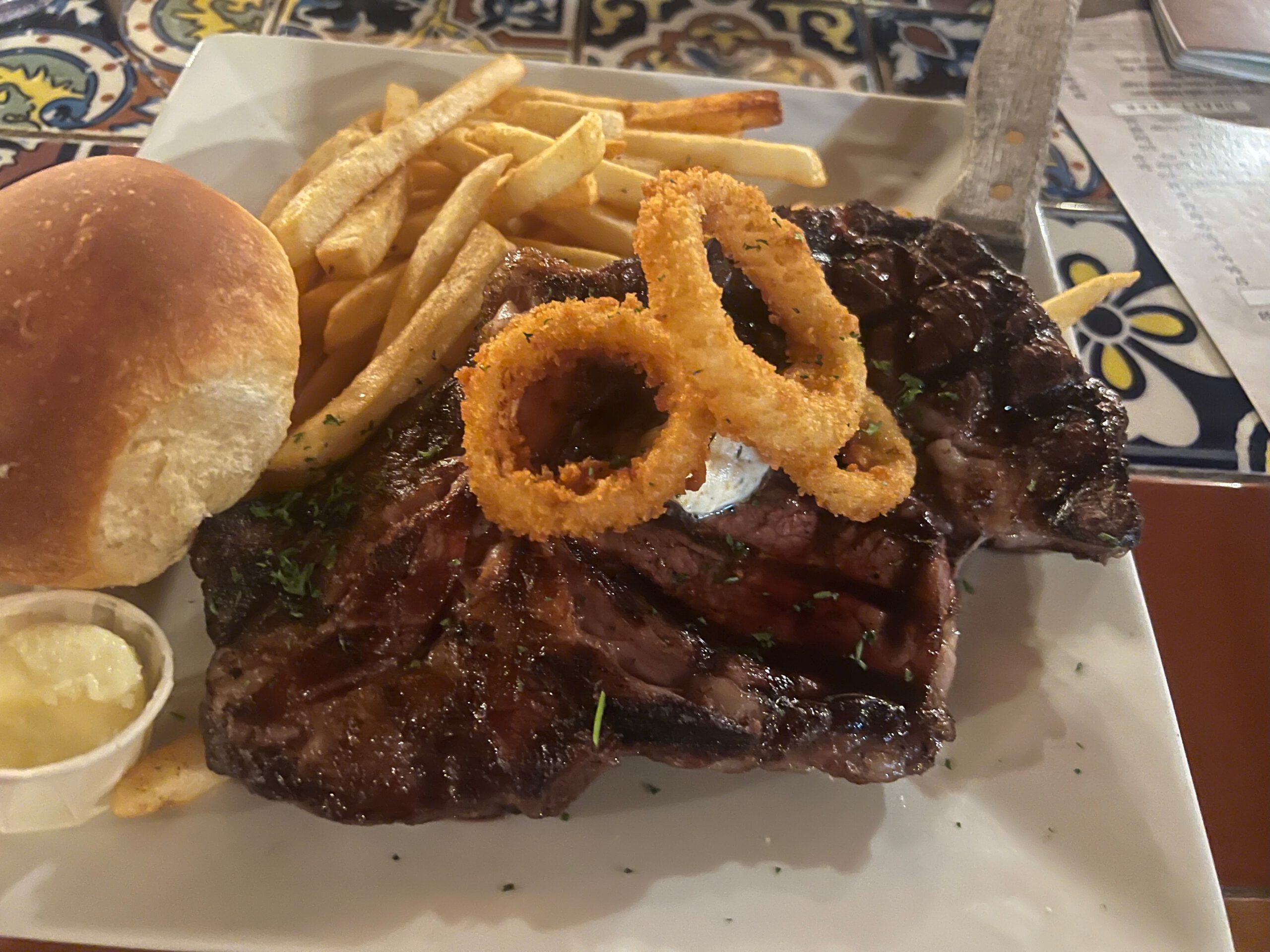 Juicy grilled steak at Iron Horse Kanab Utah topped with crispy onion rings, served with golden fries, buttered roll, and classic western sides.
