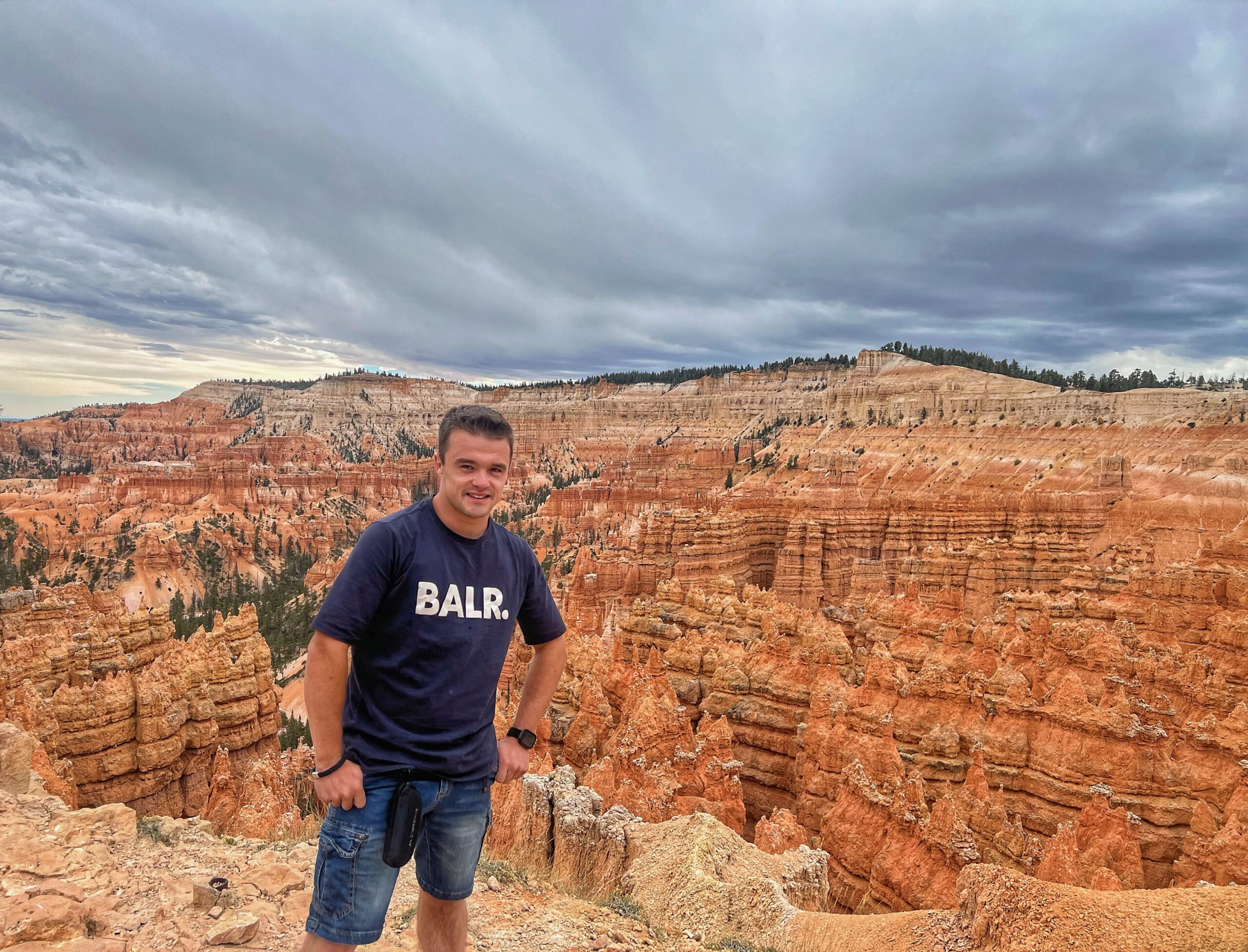 Visitor standing at a Bryce Canyon viewpoint surrounded by towering orange hoodoos and layered rock formations under a dramatic sky