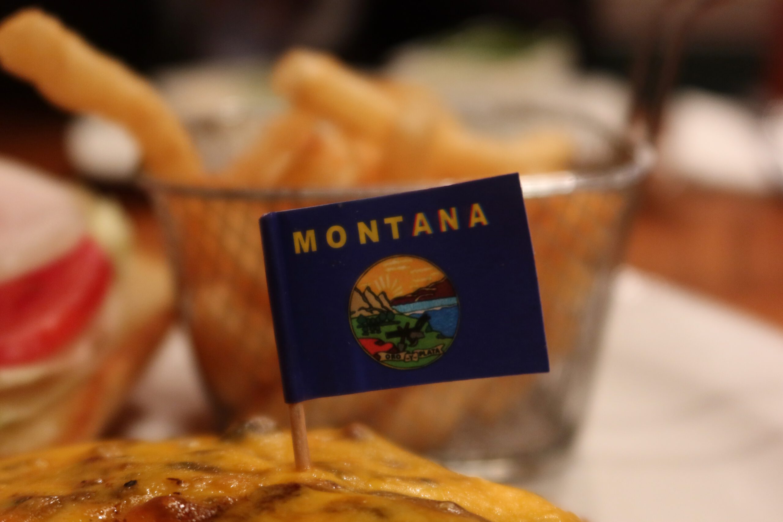 Montana burger at Cowboy’s Lodge and Grille Gardiner, topped with melted cheddar and a small Montana state flag, served with fries in a rustic Western restaurant near Yellowstone National Park