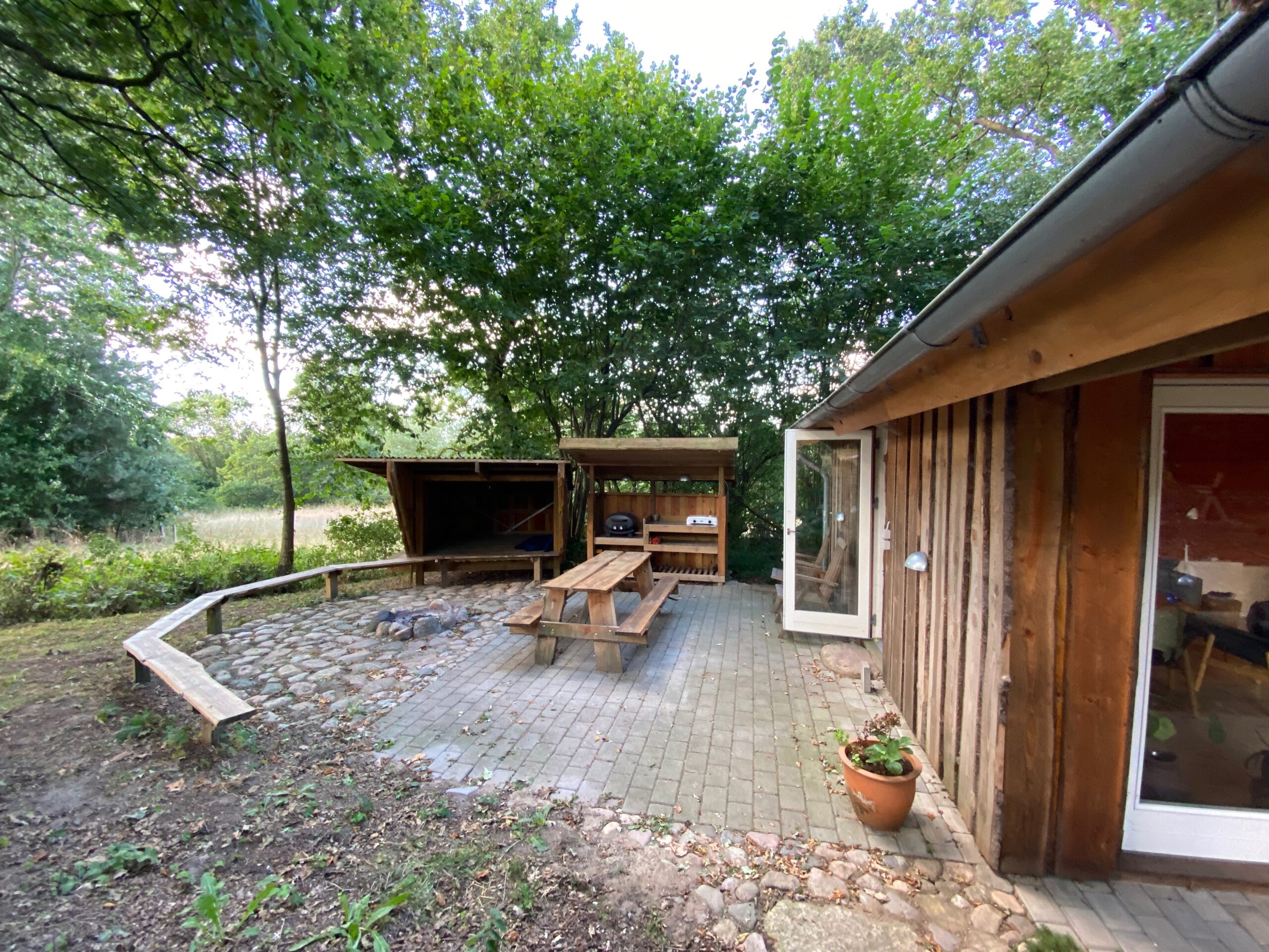 Solevad Cottage in the Forest, outdoor seating area with picnic table, fire pit and outdoor kitchen surrounded by trees near Odense, Denmark