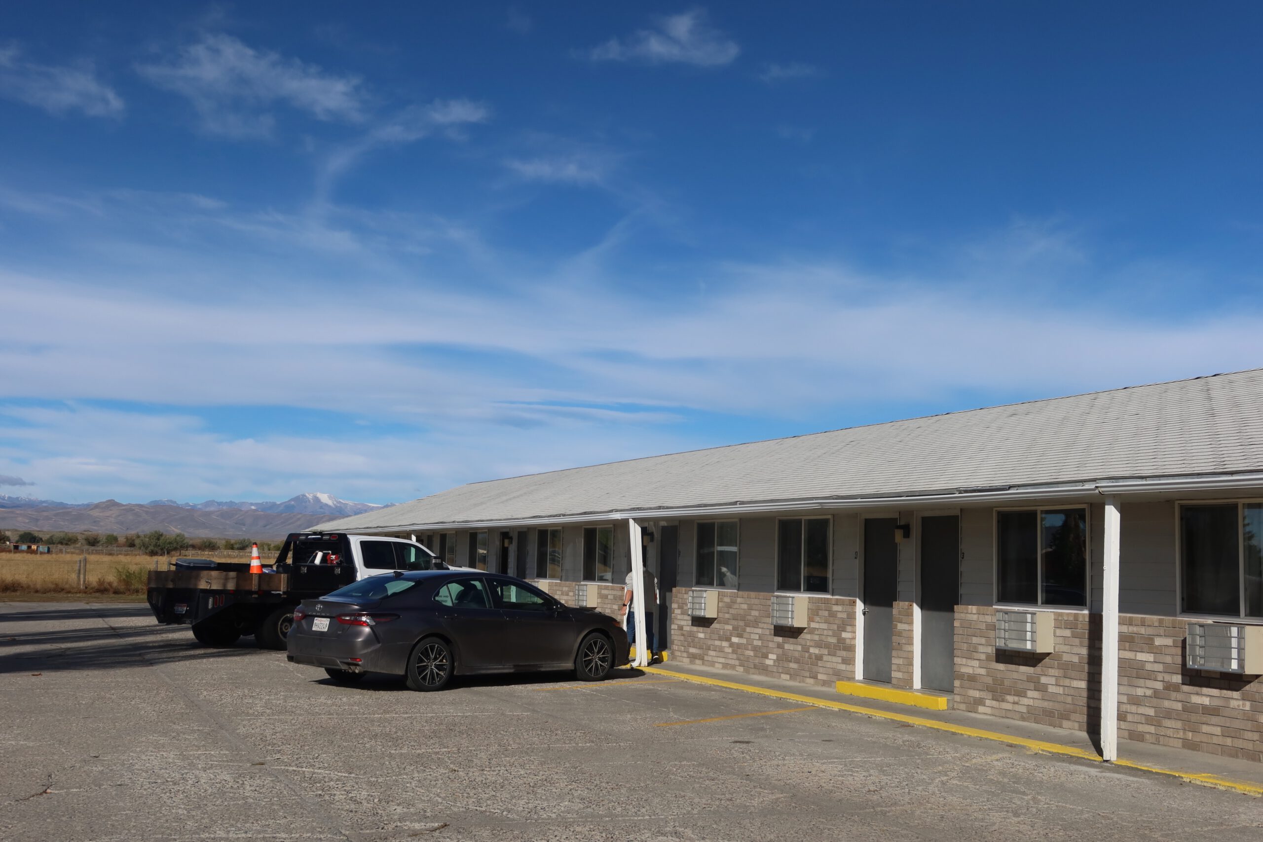 Spacious parking area at Arco Inn Motel in Idaho, showing multiple rooms with direct car access, wide open surroundings, and a clear blue sky typical of an American road trip stop