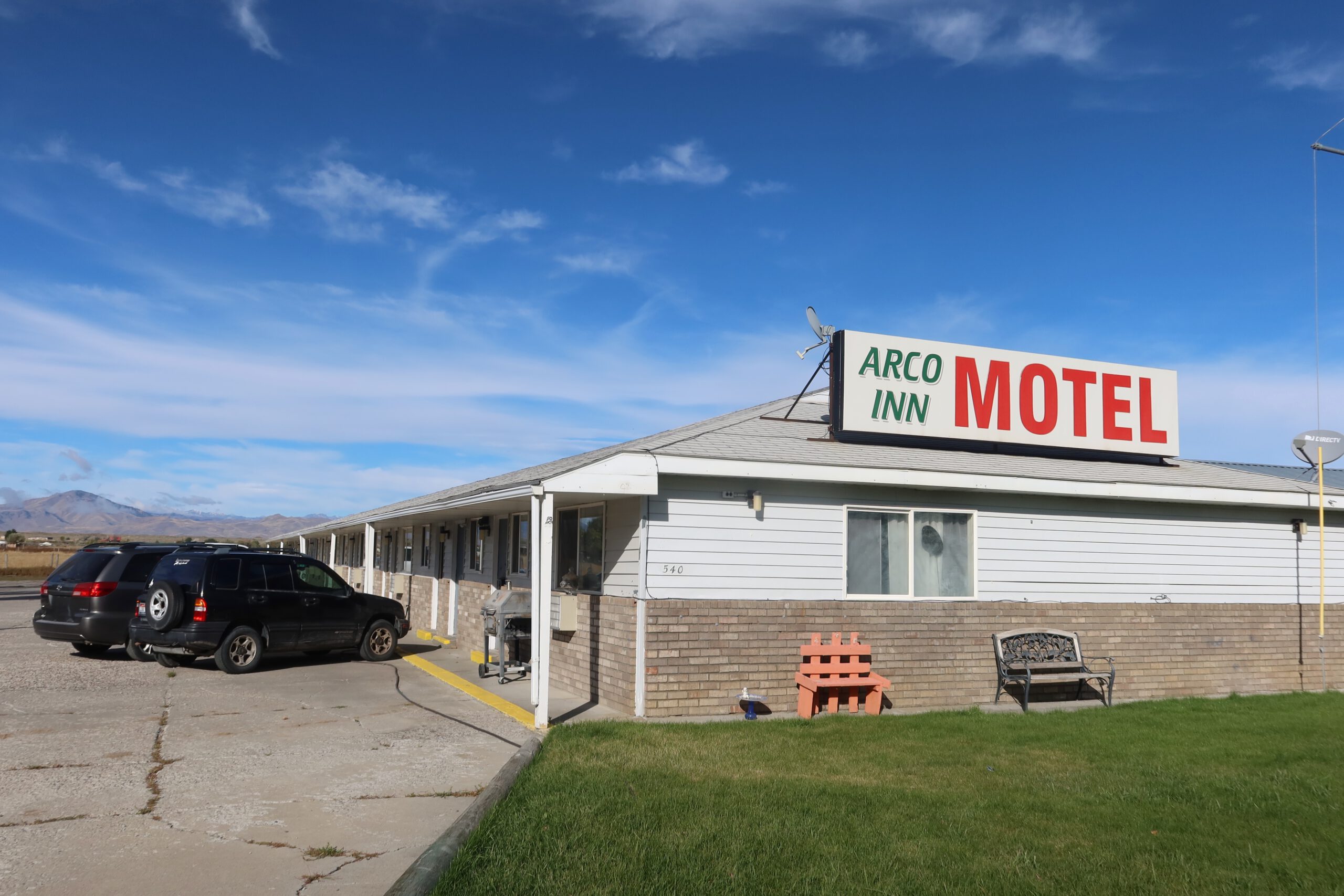 Arco Inn Motel exterior in Arco, Idaho, showing a classic American roadside motel with the iconic roof sign, free parking in front of the rooms, and wide open Idaho landscape under a bright blue sky