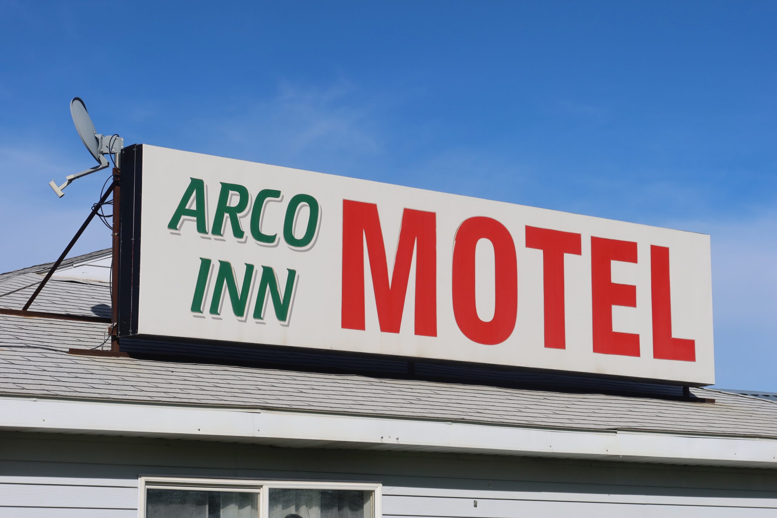 Arco Inn Motel roof sign in Arco, Idaho, featuring the classic green and red roadside motel lettering mounted on the roof against a clear blue sky