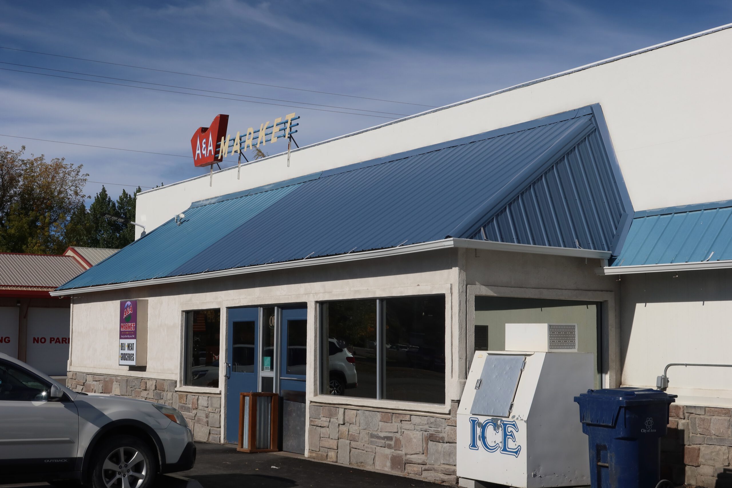 A & A Market Arco Idaho exterior with blue metal roof, parking spaces, ice freezer outside, and storefront windows in downtown Arco