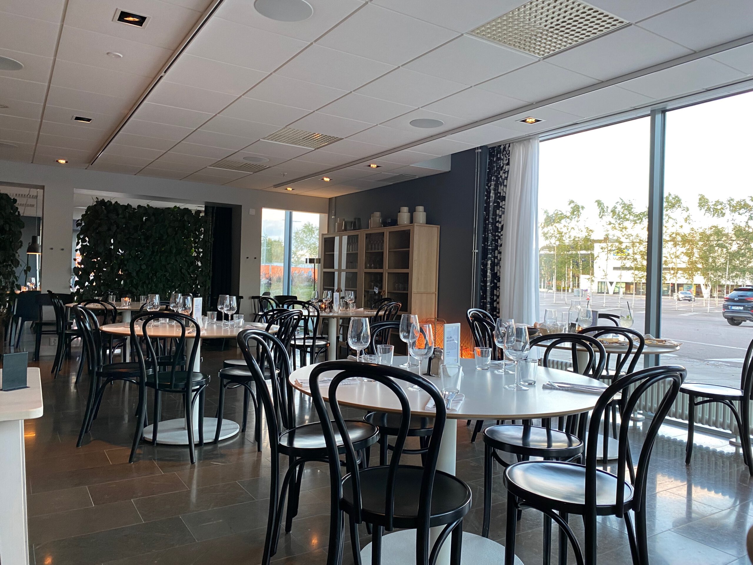 Interior of the IKEA Hotell Älmhult restaurant with modern Scandinavian design, round tables, black chairs, soft lighting and large windows overlooking the surroundings.