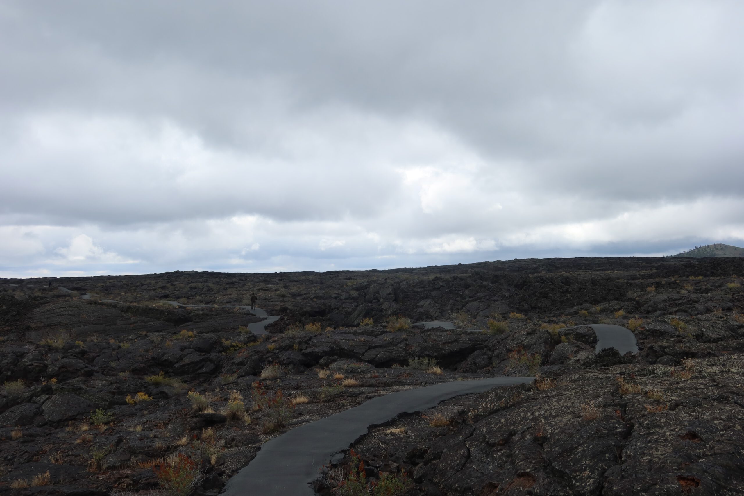 Walking path through dark lava fields at Craters of the Moon National Monument in Idaho, showing the vast volcanic landscape