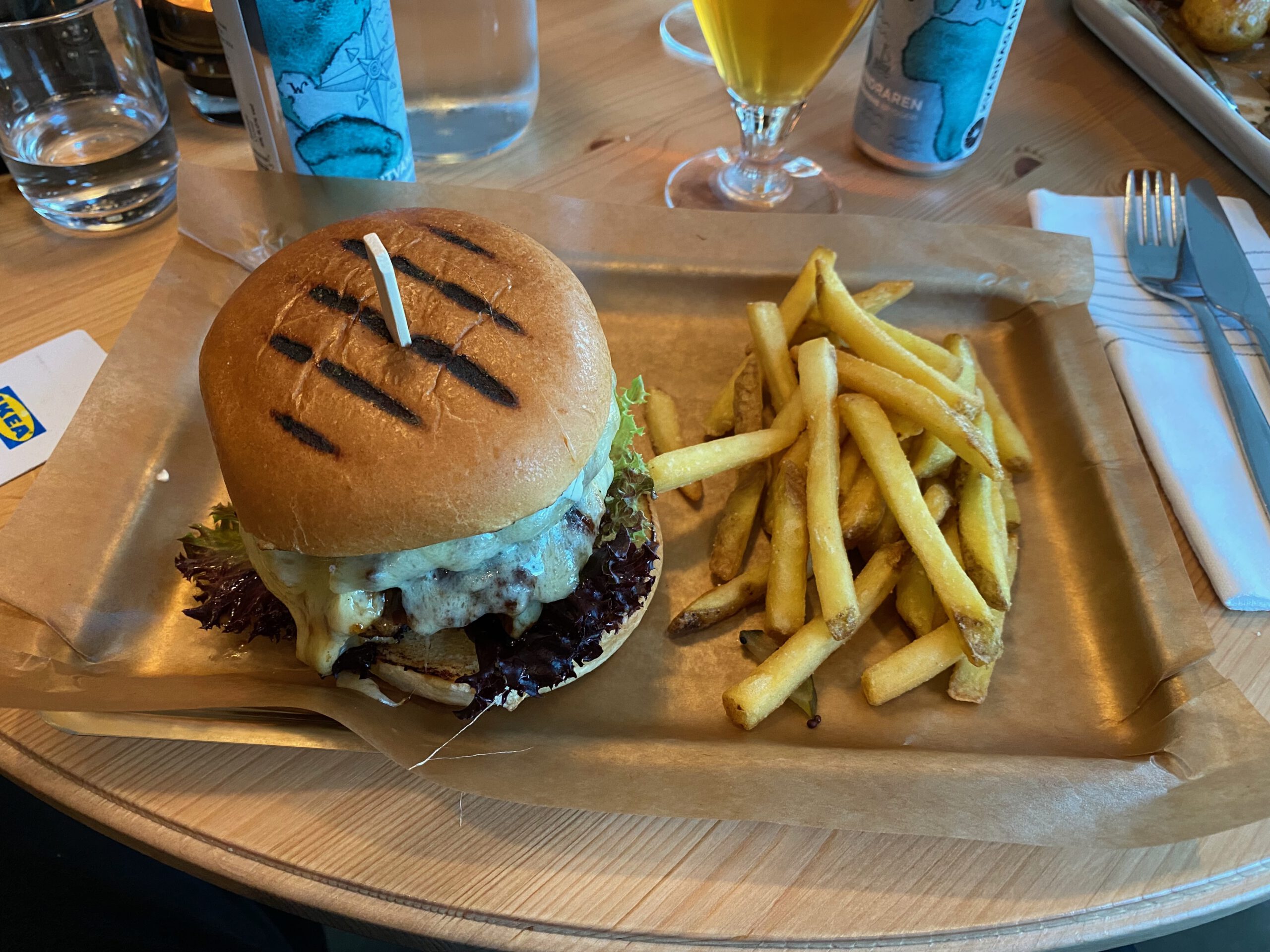 IKEA Hotell Älmhult restaurant dinner featuring a homemade beef burger with melted cheese, lettuce and creamy sauce, served on a toasted bun with crispy golden fries on a wooden table.