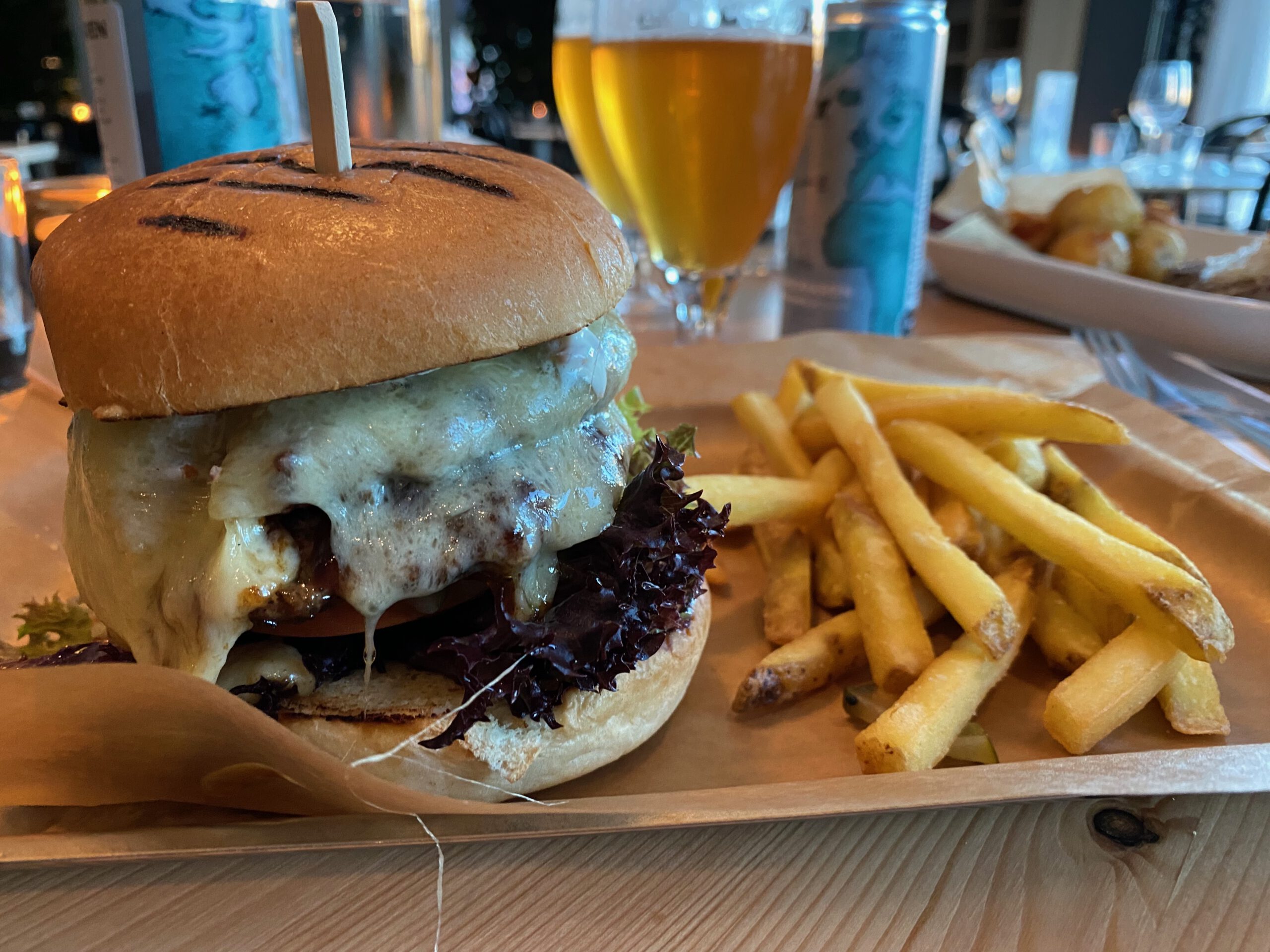 IKEA Hotell Restaurant Älmhult homemade burger topped with melted cheese, grilled beef patty, fresh leafy lettuce and crispy fries, served on a wooden table with local craft beer inside the restaurant