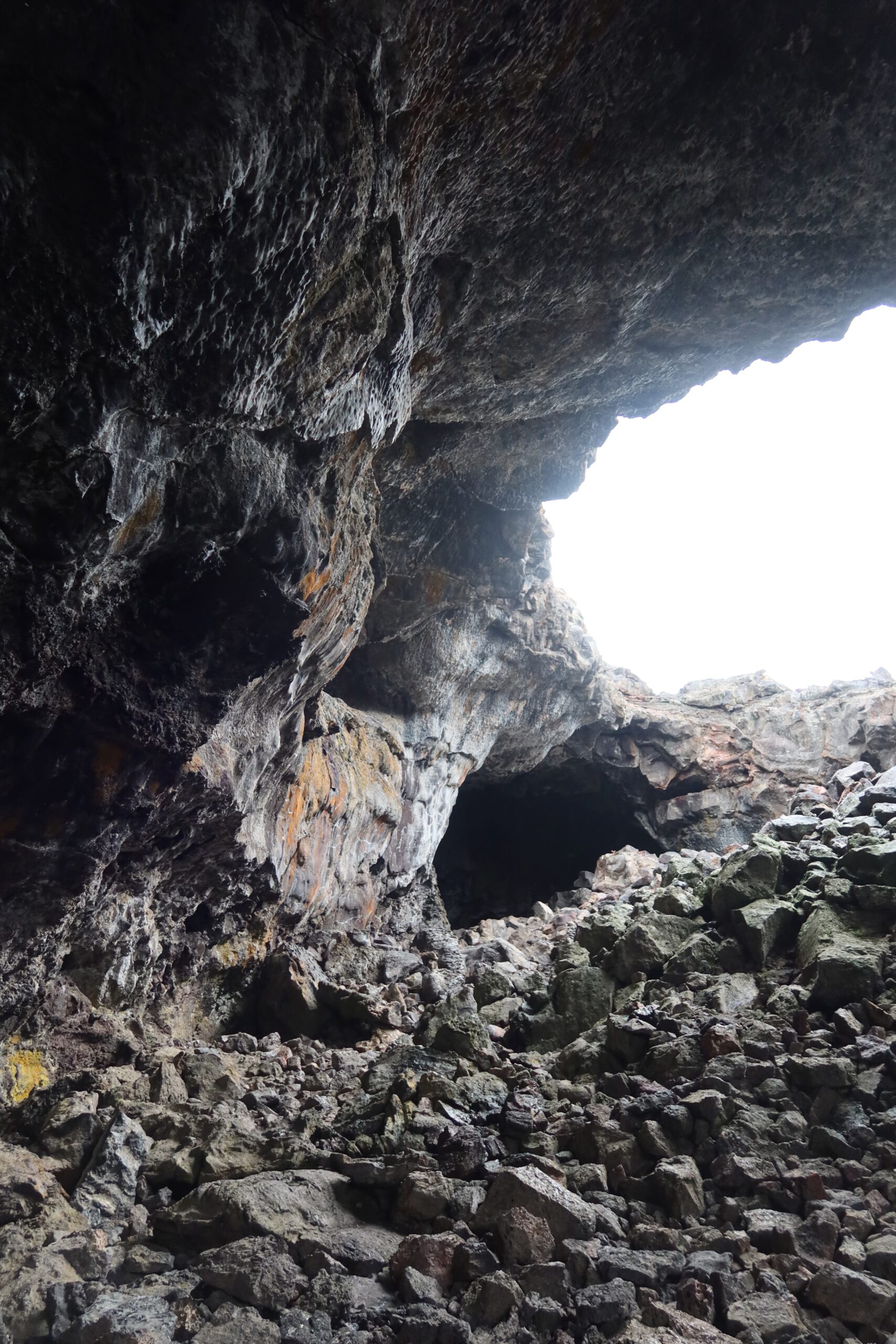 Inside the Indian Tunnel lava tube at Craters of the Moon National Monument in Idaho, showing rough volcanic rock walls and the cave opening above