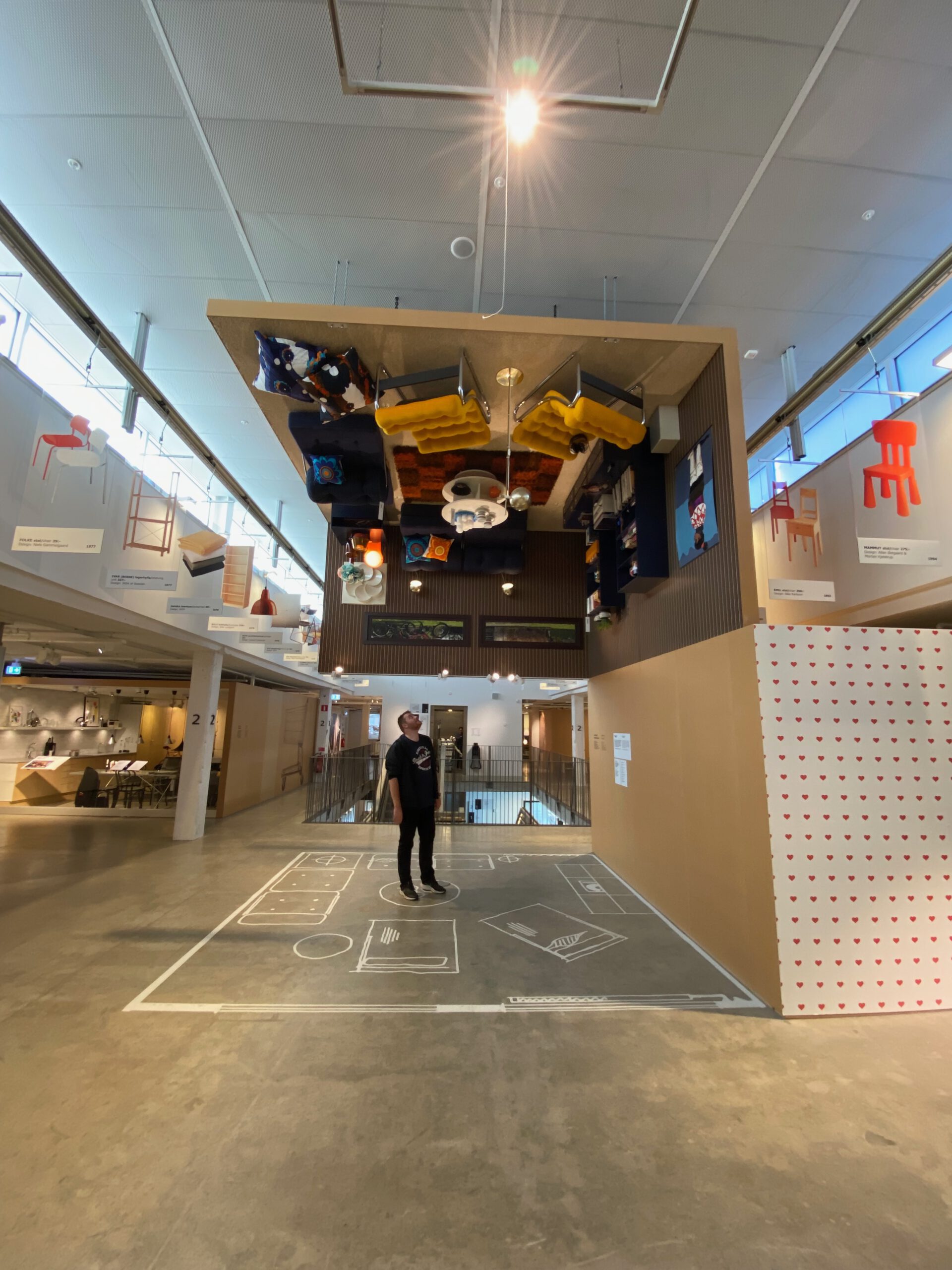 IKEA Museum Älmhult, Timo van den Berg stands around interior with iconic upside-down room installation, showing floating furniture and playful design history exhibit