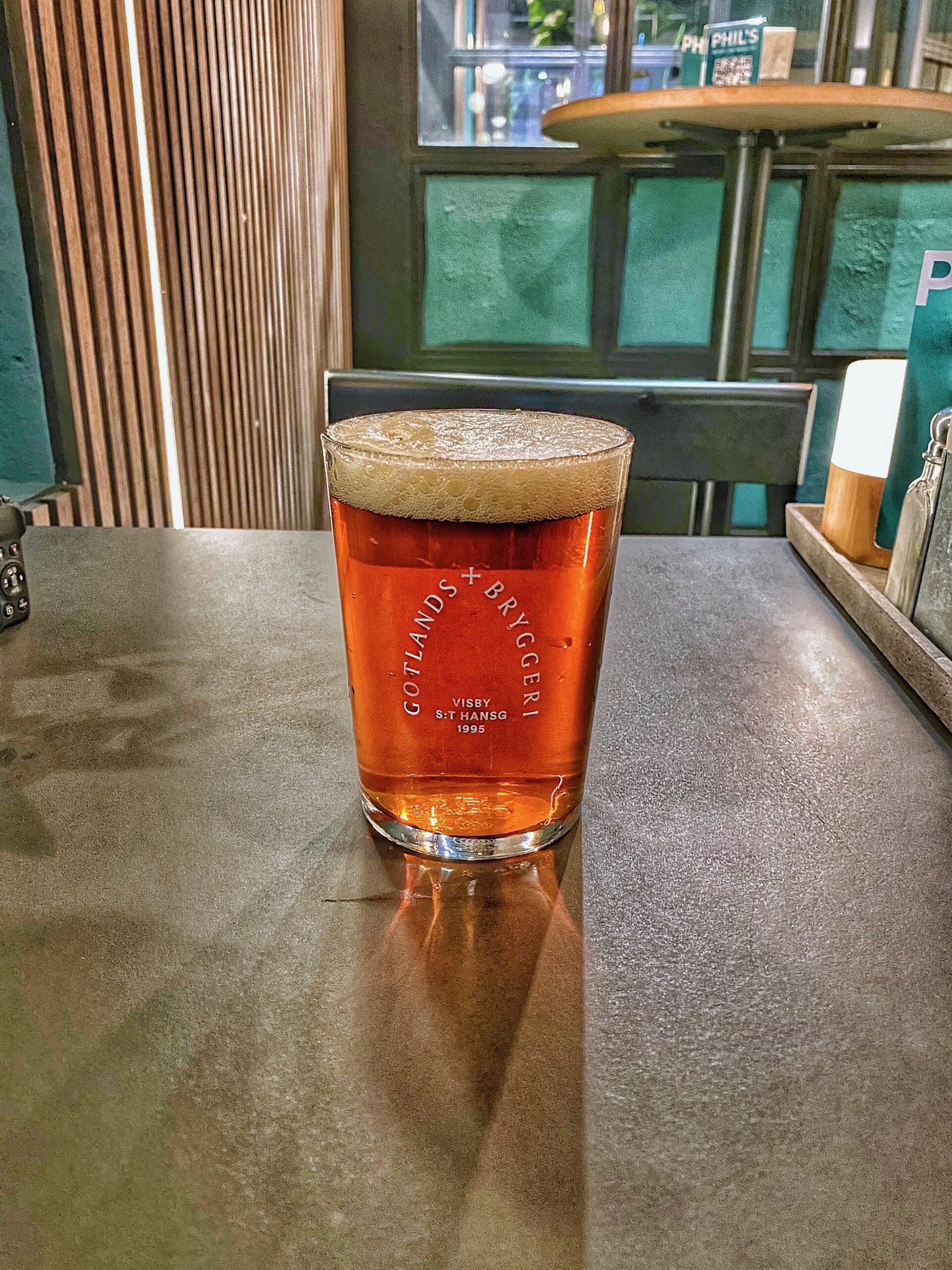 Phils Burger Drottninggatan Stockholm serving a Gotlands Bryggeri craft beer, shown as an amber-colored Swedish ale with a creamy foam head, placed on the table inside the restaurant