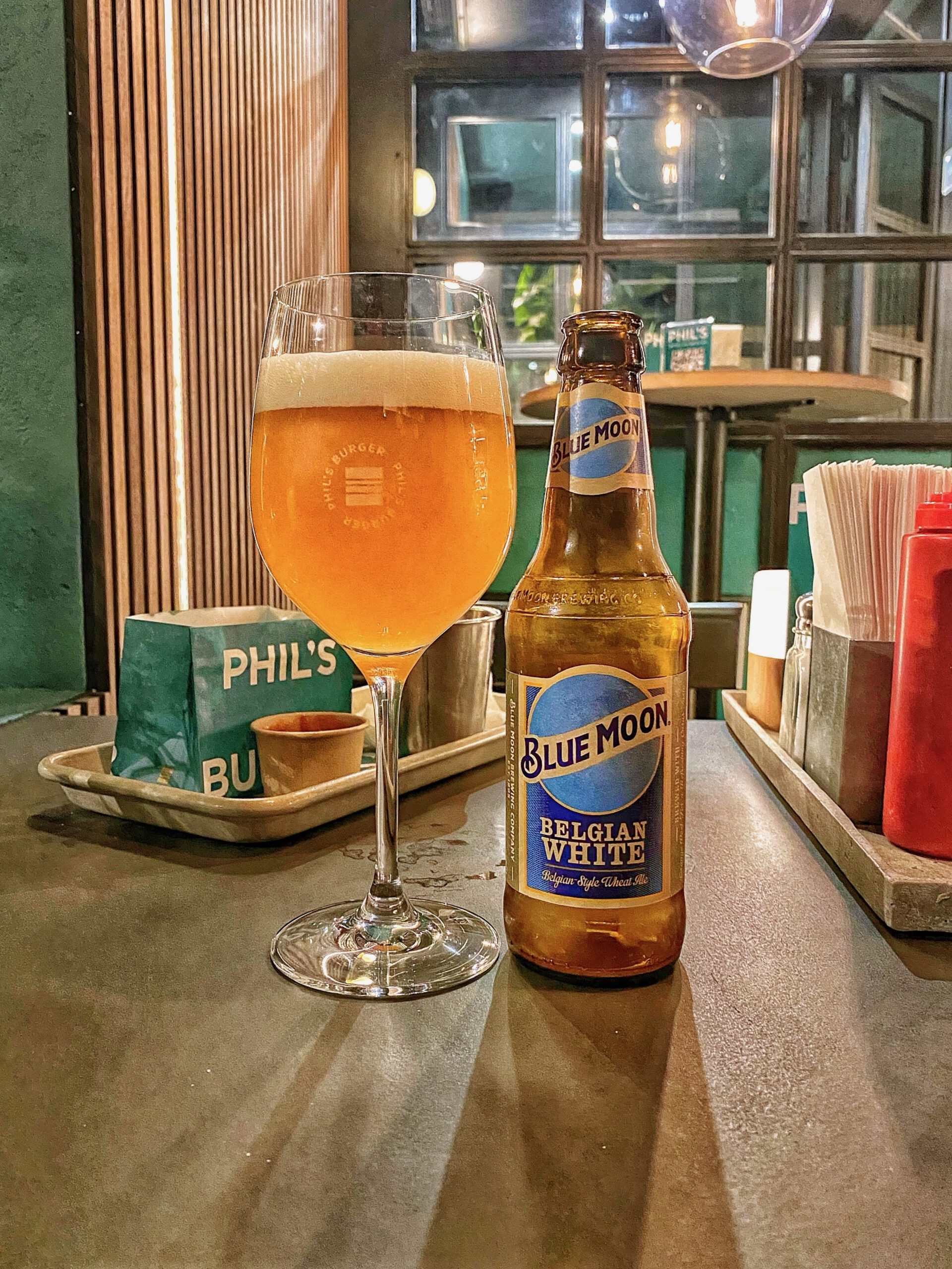 Phils Burger Drottninggatan Stockholm serving a Blue Moon Belgian White wheat beer, shown as a bottled Belgian-style witbier next to a filled beer glass inside the restaurant