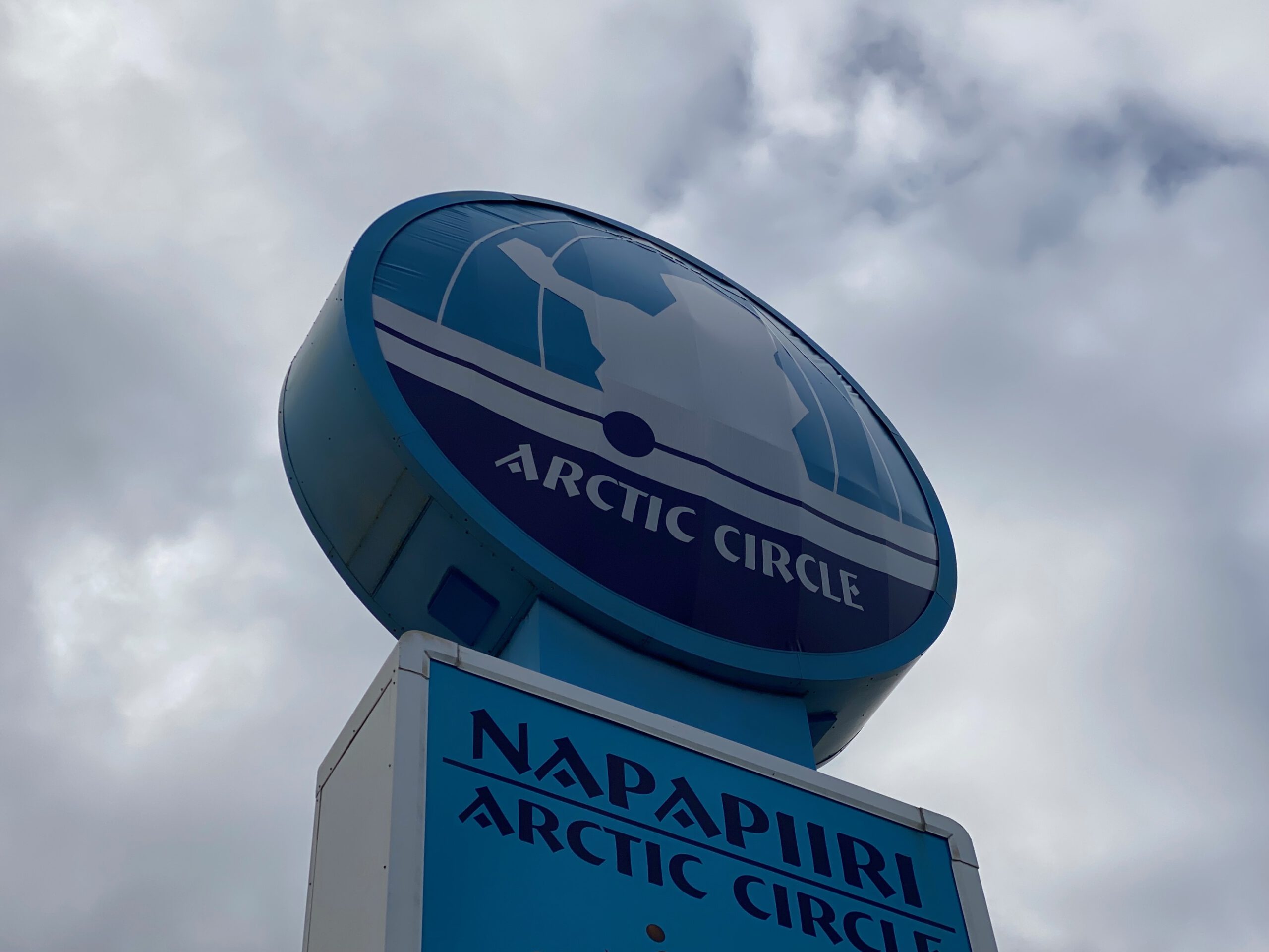Arctic Circle Tuomaan Tupa Finland, iconic blue Napapiiri Arctic Circle sign along the E8 road near Juoksenki, marking the official Arctic Circle crossing in Finnish Lapland under dramatic northern skies