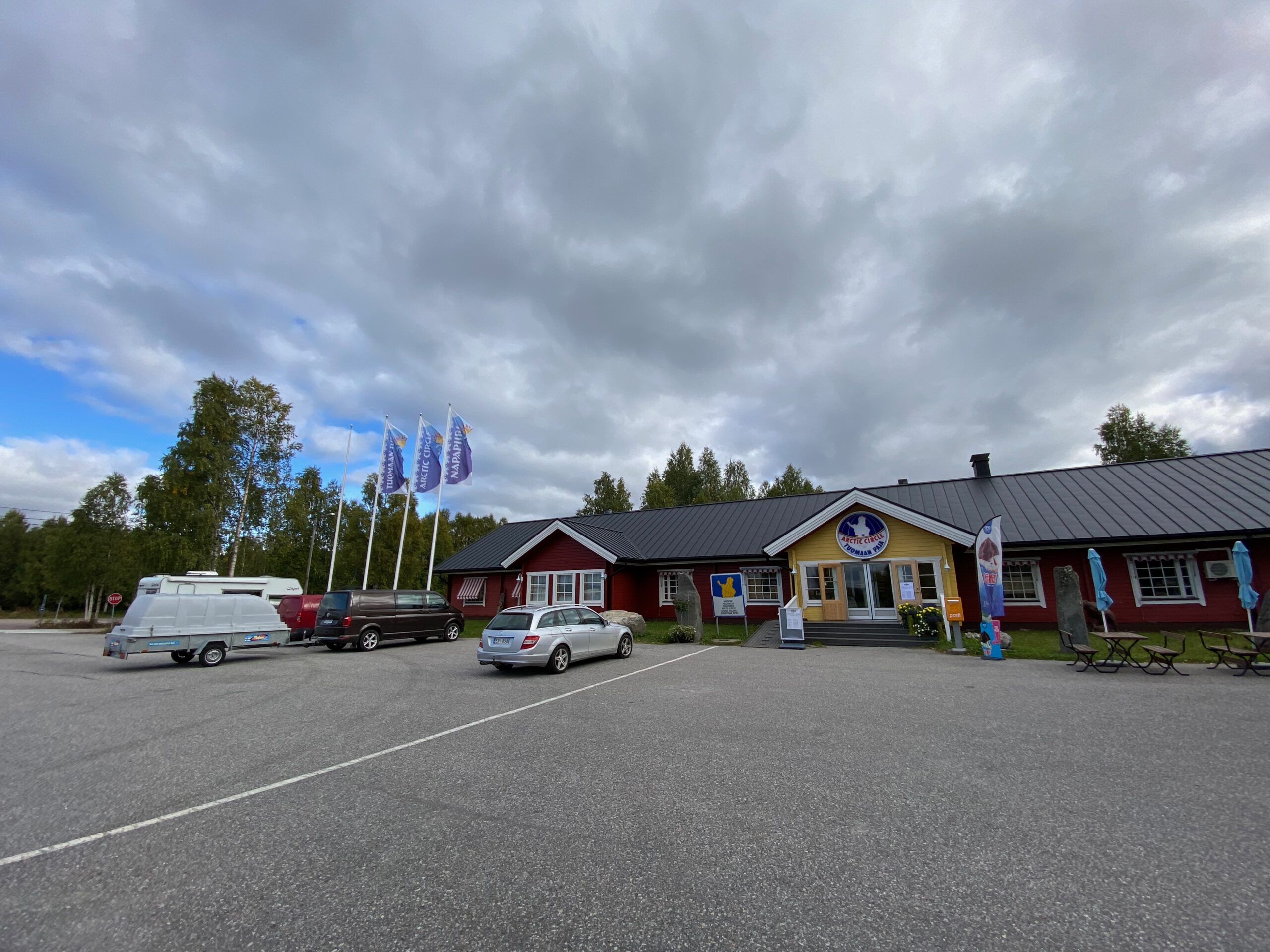 Arctic Circle Tuomaan Tupa Finland, exterior view of the iconic Arctic Circle visitor center along the E8 road in Juoksenki, Lapland, with parking area, flags, and dramatic northern sky during a road trip stop