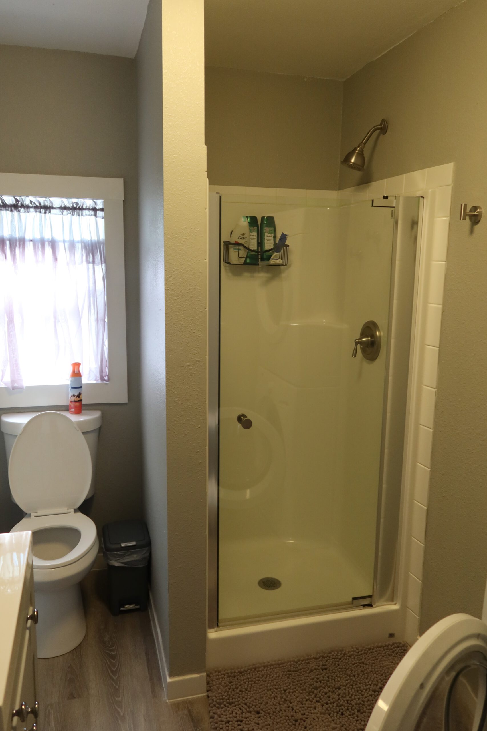 Simple bathroom in the Airbnb John Day Oregon featuring a walk in shower with glass door, toilet next to a small window, light colored walls, and practical layout for a short stay.