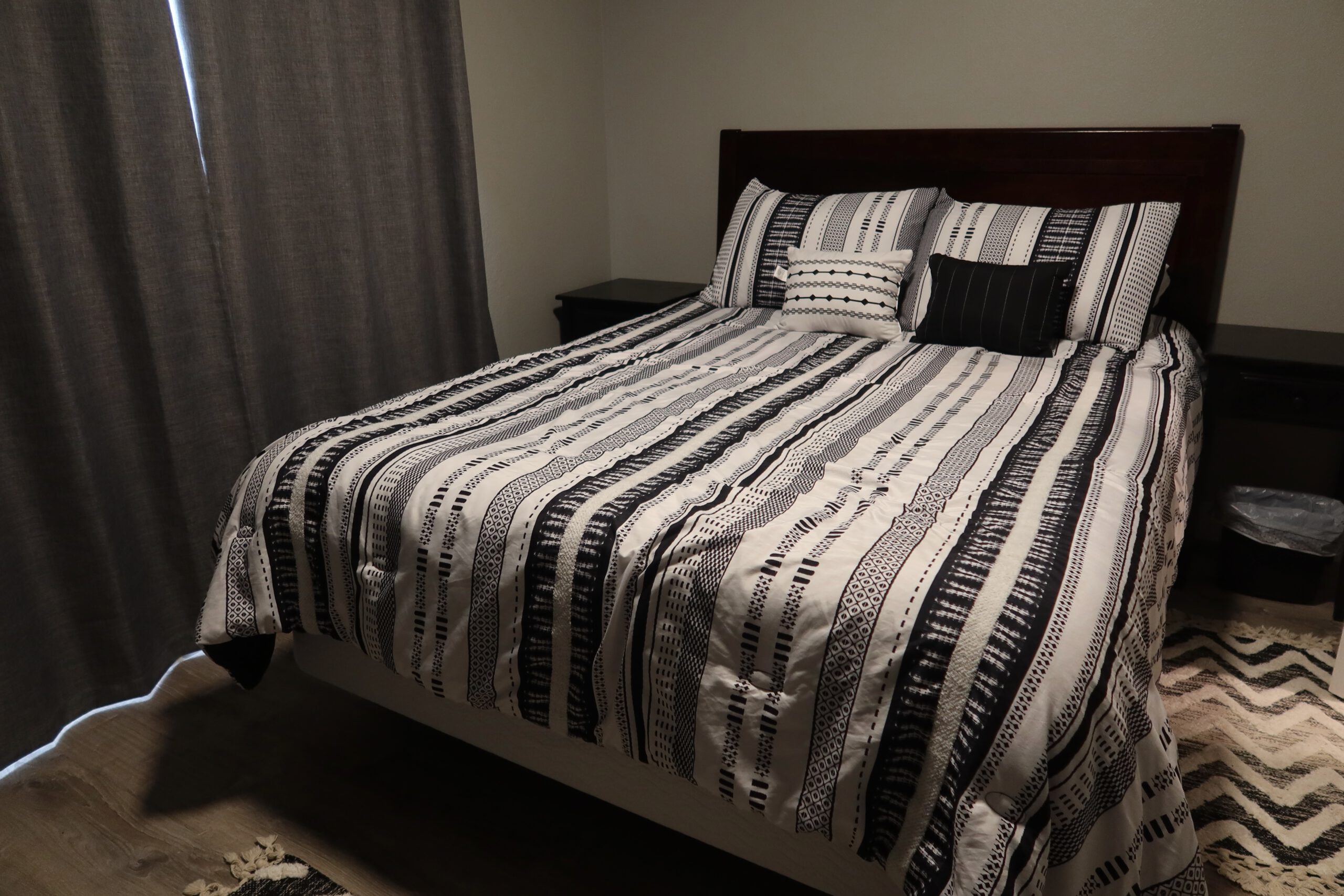 Queen size bed in the Airbnb John Day Oregon bedroom, made with patterned black and white bedding, matching pillows, bedside tables, and dark curtains creating a simple and calm sleeping space.