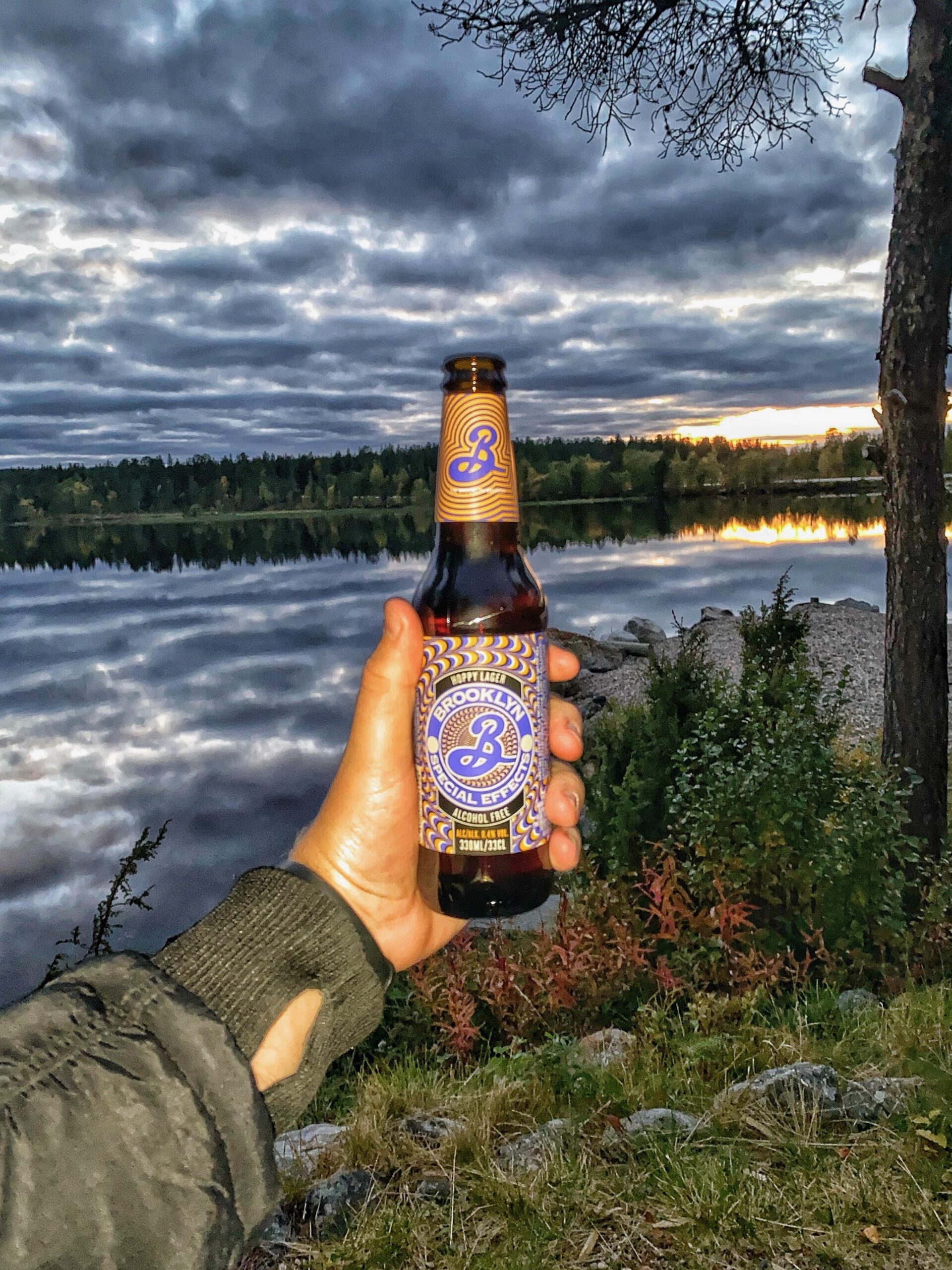 Brooklyn Special Effects alcoholvrij bier van Brooklyn Brewery, gefotografeerd aan een spiegelend meer bij Hetan Kota in Enontekiö, Finland, met dramatische wolkenlucht en serene Laplandse wildernis.