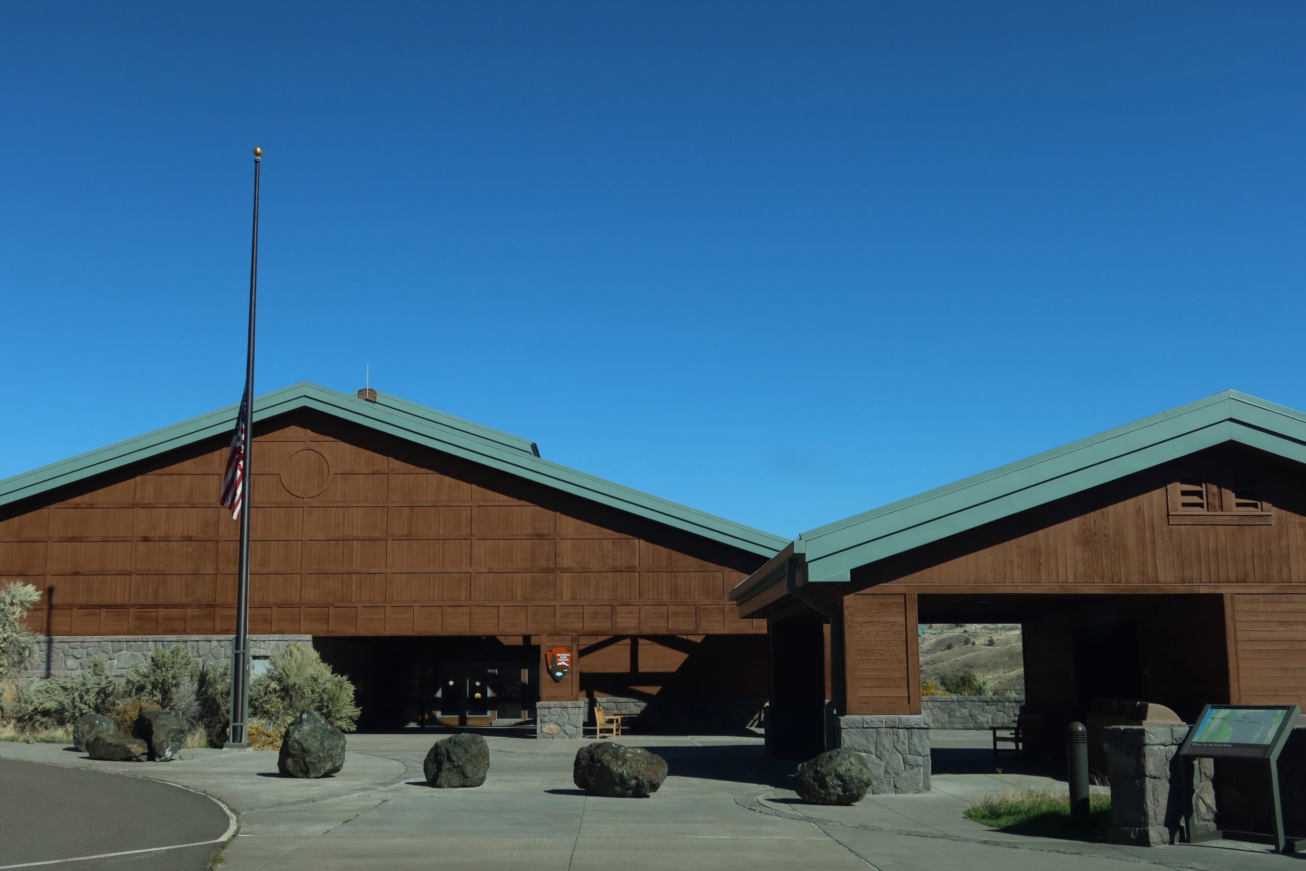Wide view of the John Day Fossil Beds National Monument visitor center complex featuring timber buildings, stone details, and open plaza in Eastern Oregon