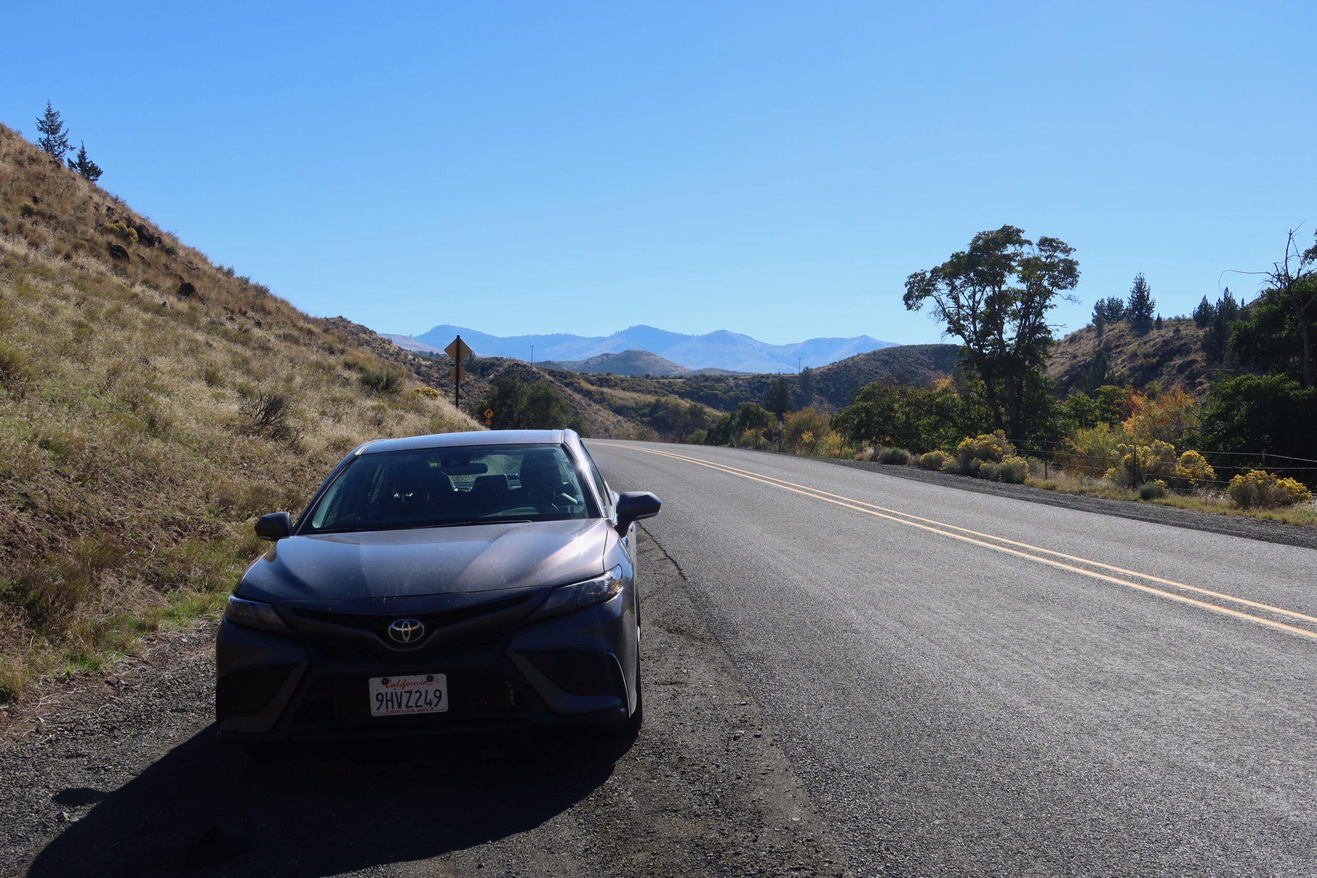 Roadside viewpoint in eastern Oregon near John Day Fossil Beds, featuring a parked car along a quiet highway with rolling hills, distant mountains, and wide open landscapes typical of rural Oregon.