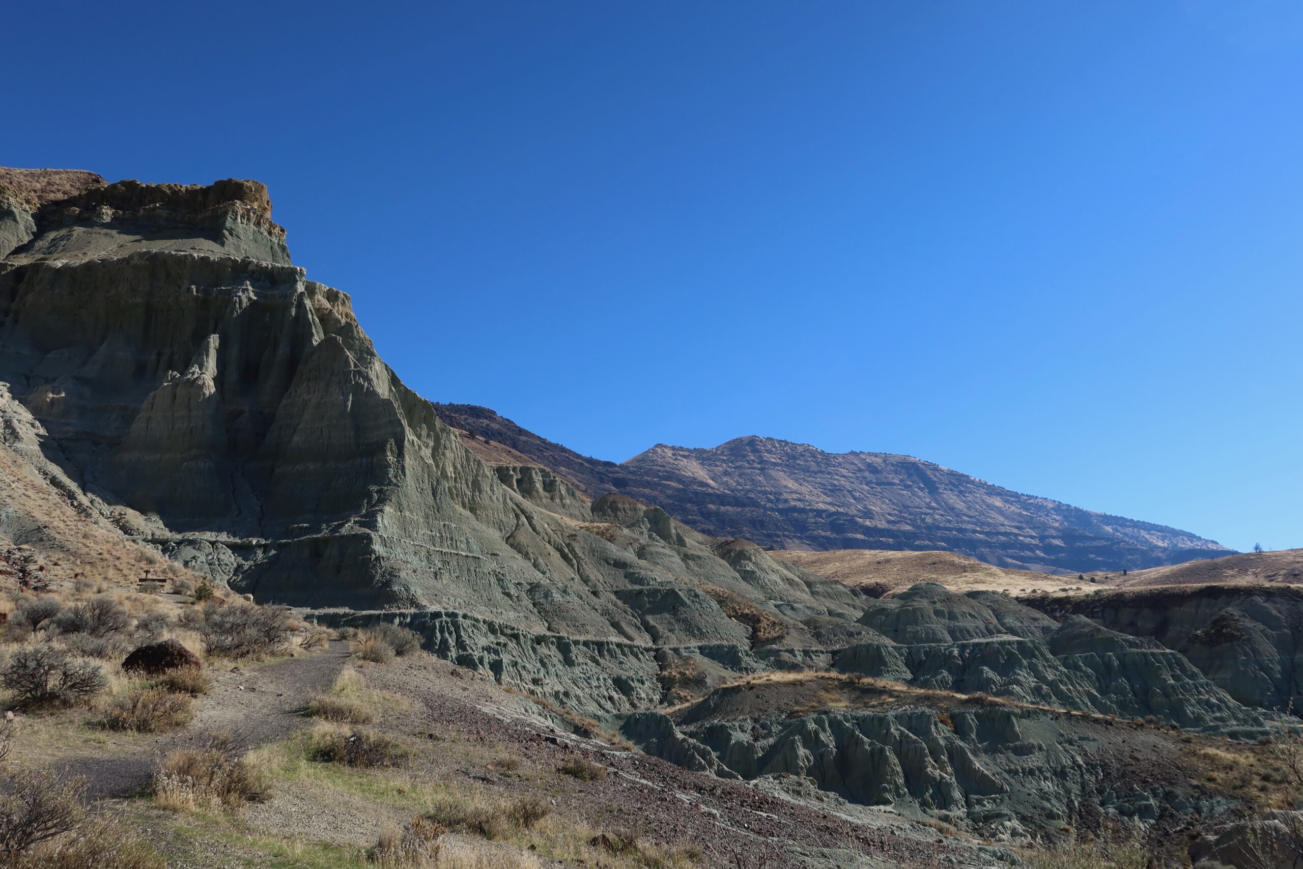 Wide roadside viewpoint of rolling hills, rocky ridges, and pine-dotted valleys in central Oregon, capturing the vast and remote John Day Fossil Beds scenery.