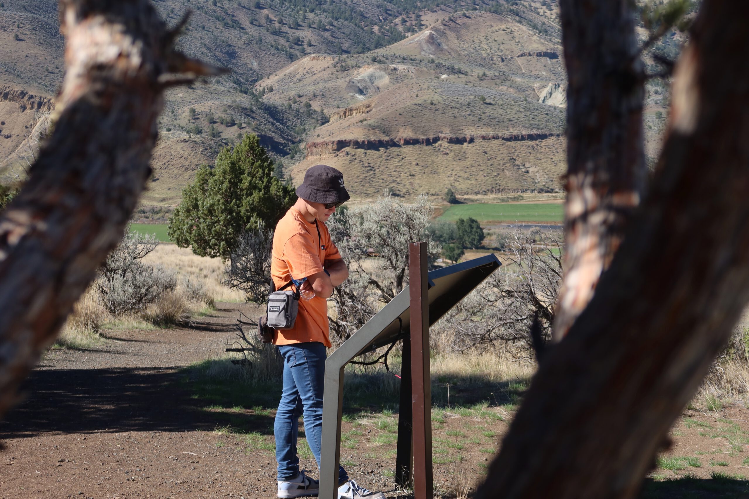 Peter Smit (peter010boy) reading an interpretive information panel along a hiking trail in John Day Fossil Beds National Monument, surrounded by rugged Oregon hills and open valley landscapes.