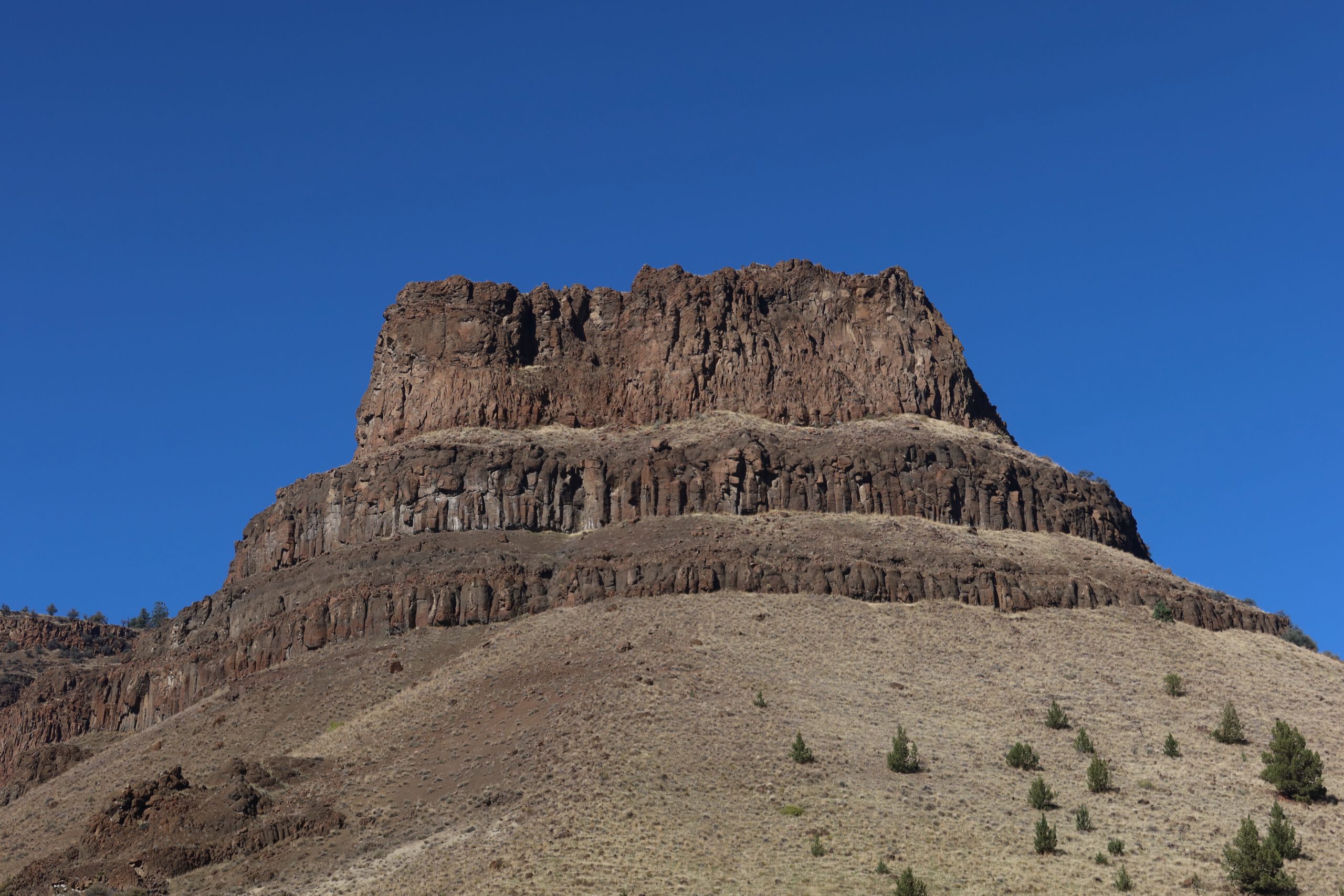 Distinctive stepped basalt formation rising from dry grassland hills in Oregon, highlighting the geological layers of the John Day region.
