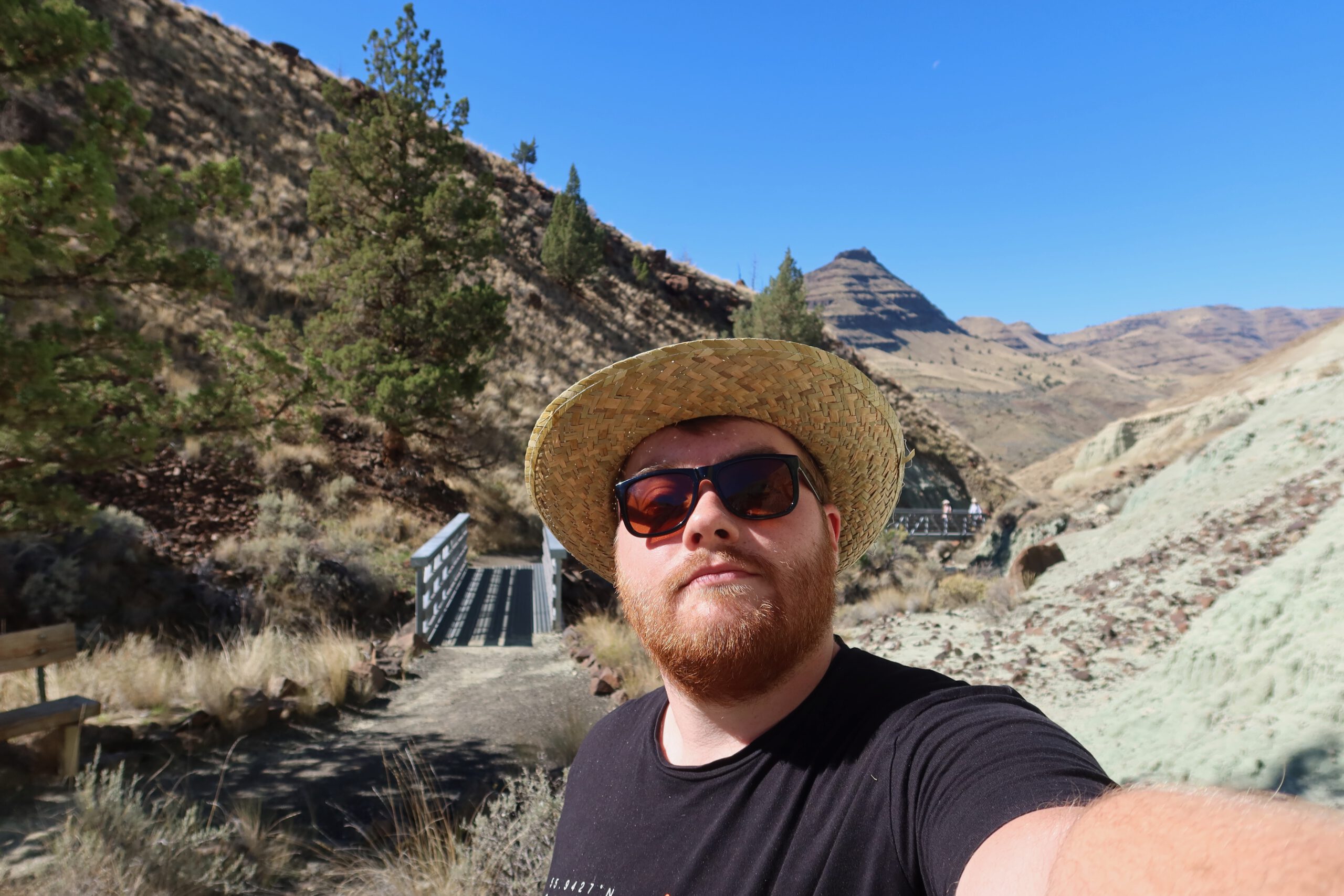 Timeuw, also known as Timo van den Berg, taking a selfie at the start of the Island in Time Trail in the Sheep Rock Unit of John Day Fossil Beds National Monument, with layered volcanic hills and a footbridge in the background