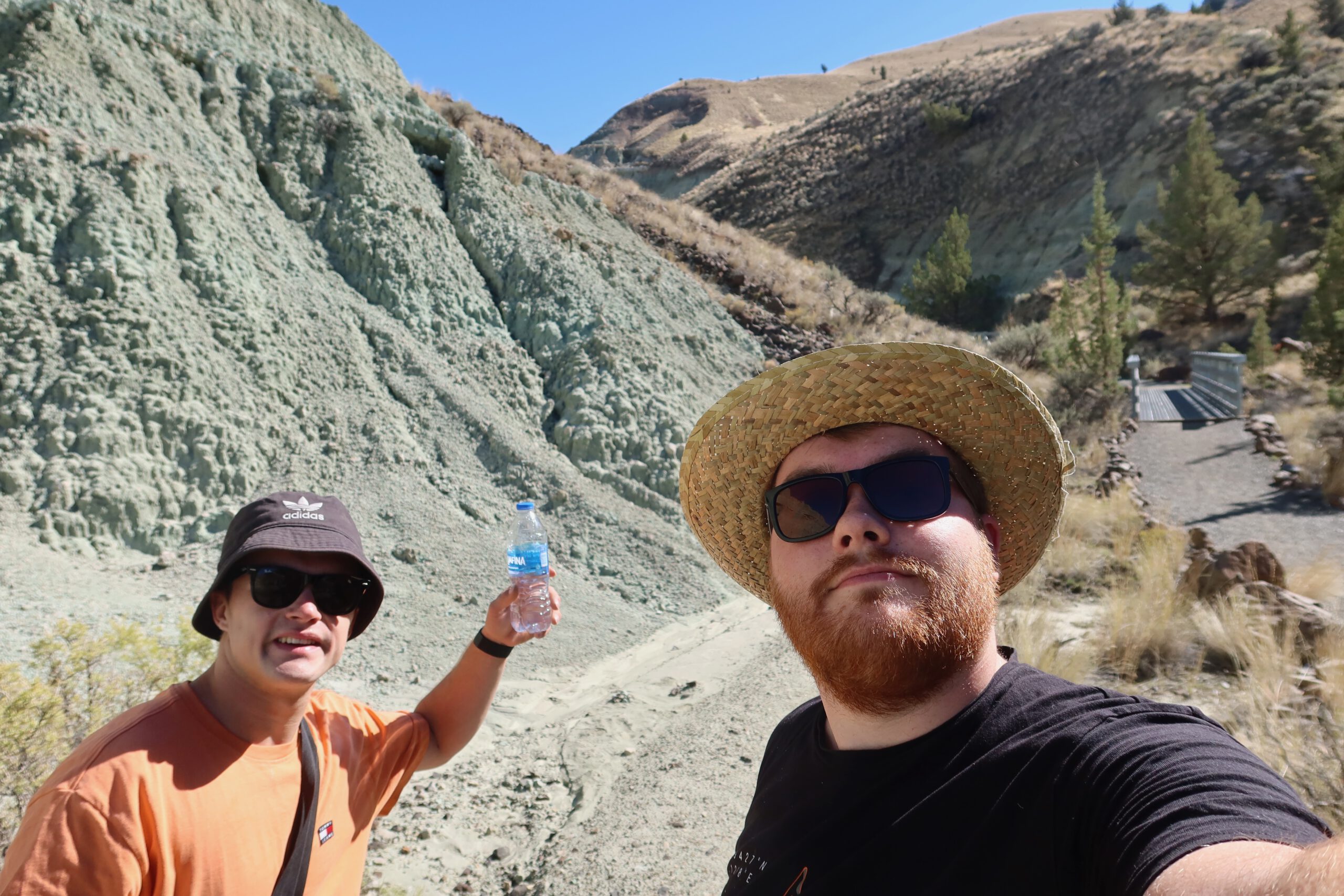 Timo van den Berg and Peter Smit taking a break during a hike at John Day Fossil Beds National Monument, standing among green clay hills and volcanic badlands in Eastern Oregon