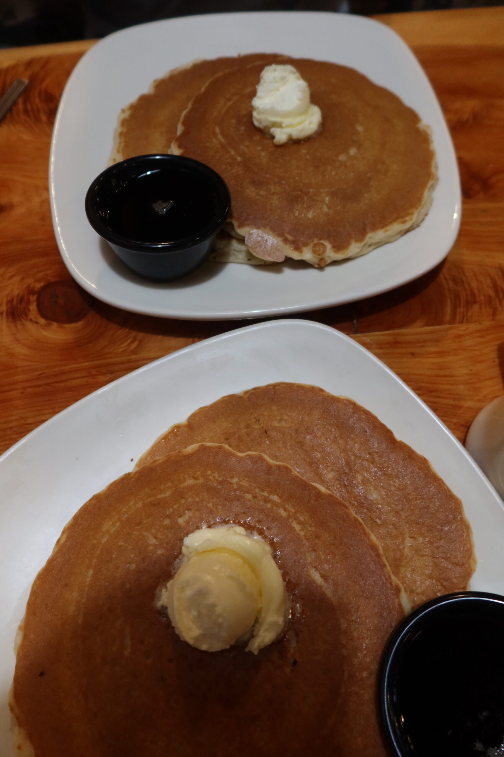 Stack of golden pancakes served with butter and maple syrup at Outpost Pizza Pub & Grill John Day, presented on a white plate on a wooden table, showcasing a classic American breakfast option in John Day, Oregon.