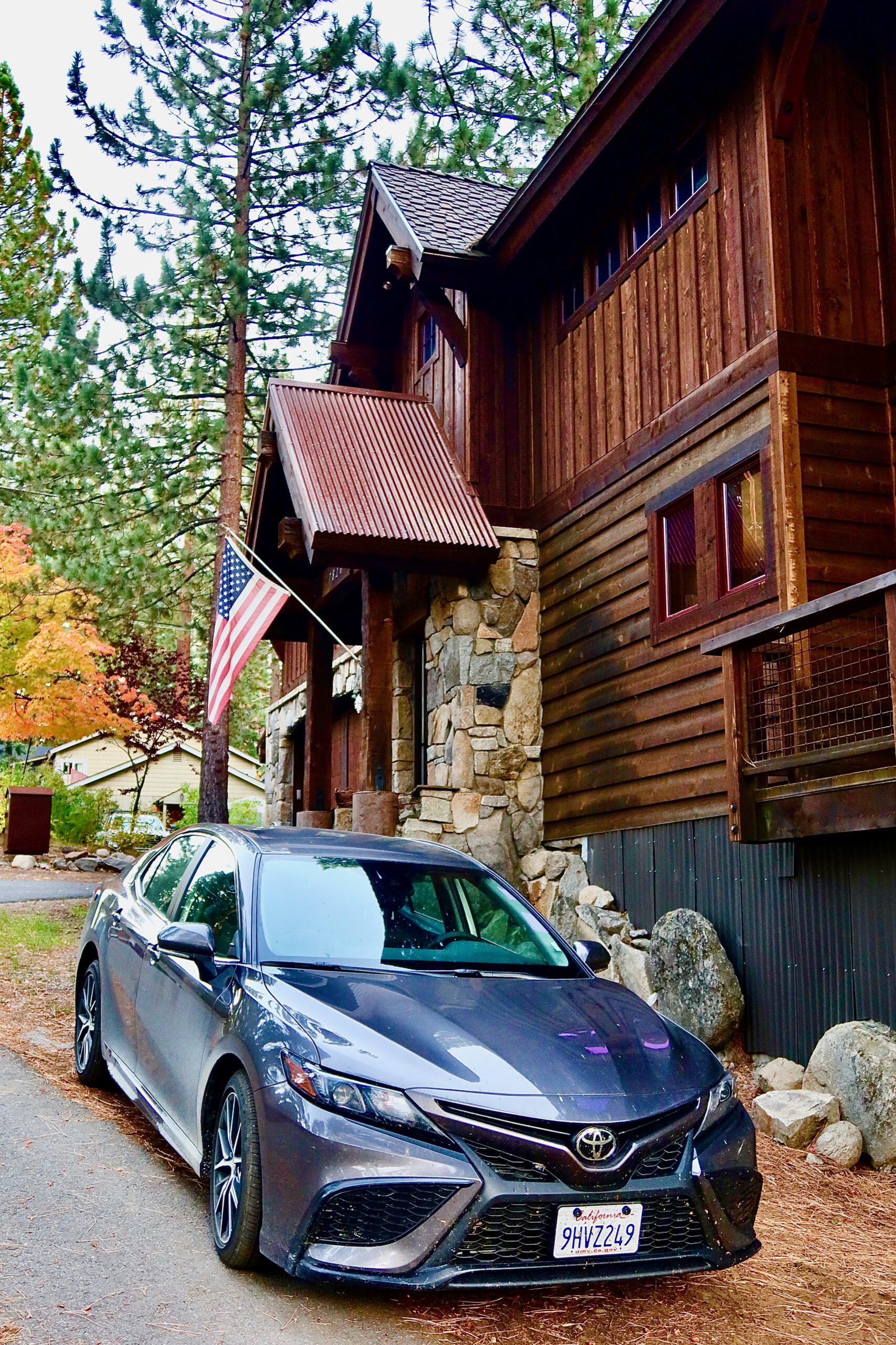 Gray Toyota Camry parked in front of a rustic wooden cabin in Tahoe Vista, part of a Lake Tahoe studio rental, surrounded by pine trees and a quiet North Lake Tahoe neighborhood, next to our Airbnb.