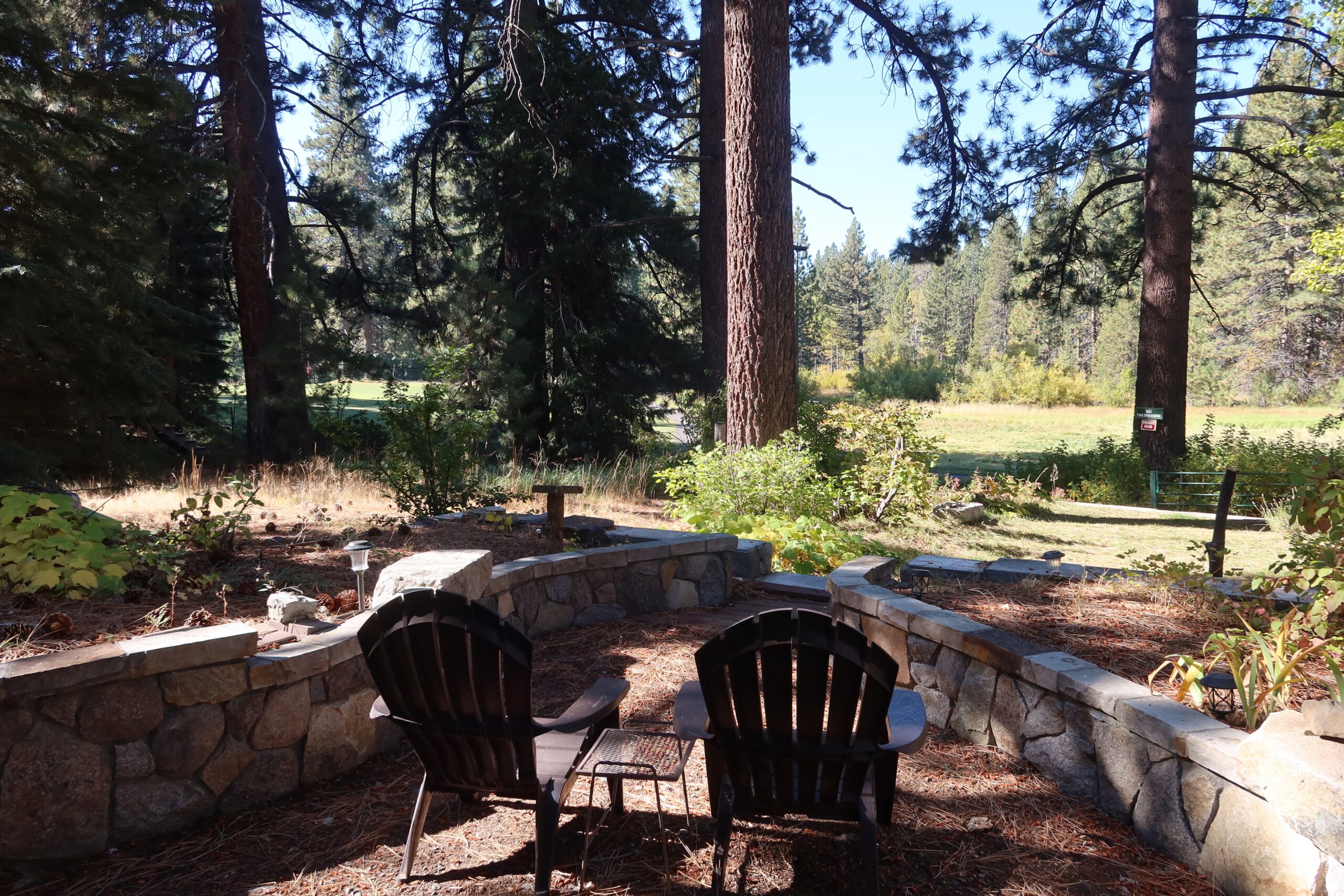 Outdoor seating area with Adirondack chairs surrounded by pine trees and stone walls, offering a peaceful forest view near a Lake Tahoe studio rental beside a golf course.