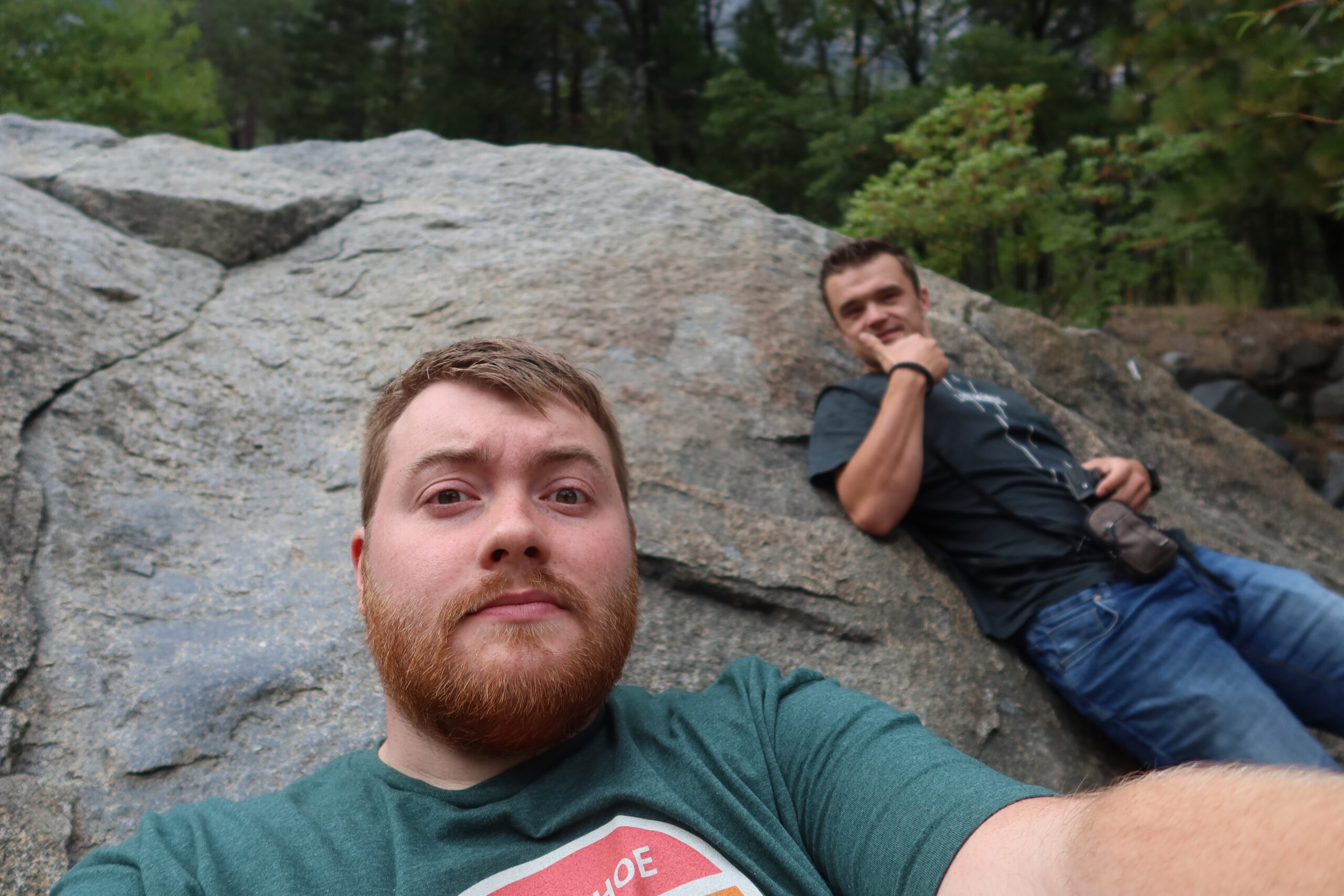 Yosemite National Park viewpoint with two travelers sitting on a large granite rock surrounded by forest, capturing a relaxed moment during a national park visit