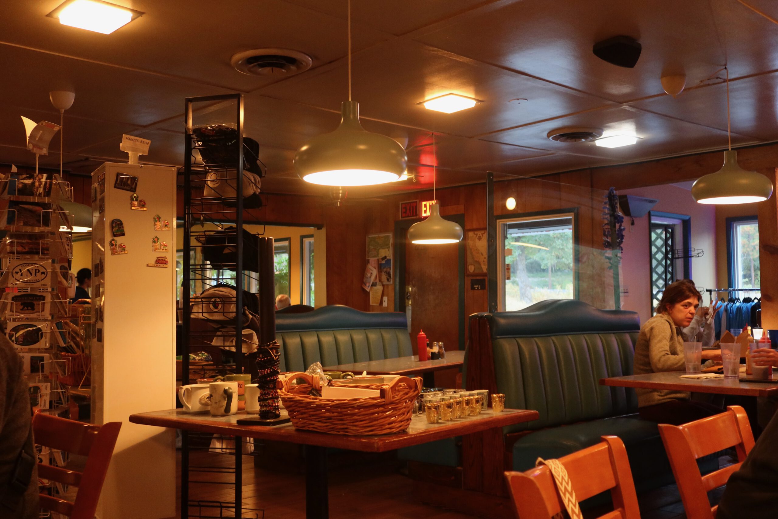 Interior of Lucky Buck Cafe California with teal vinyl booths, wooden tables, hanging pendant lights, condiment baskets, and guests dining inside a classic American diner near Yosemite.