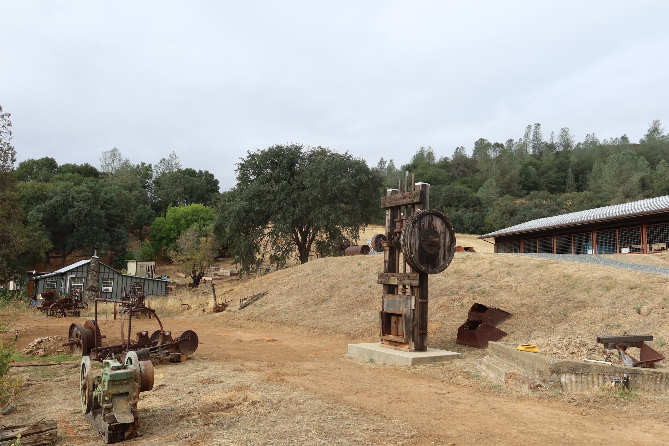 Historic mining equipment displayed outdoors at the Coulterville History Center along CA 49 in Coulterville, California, showing old gold rush era machinery surrounded by dry hills and oak trees in Northern Mariposa County