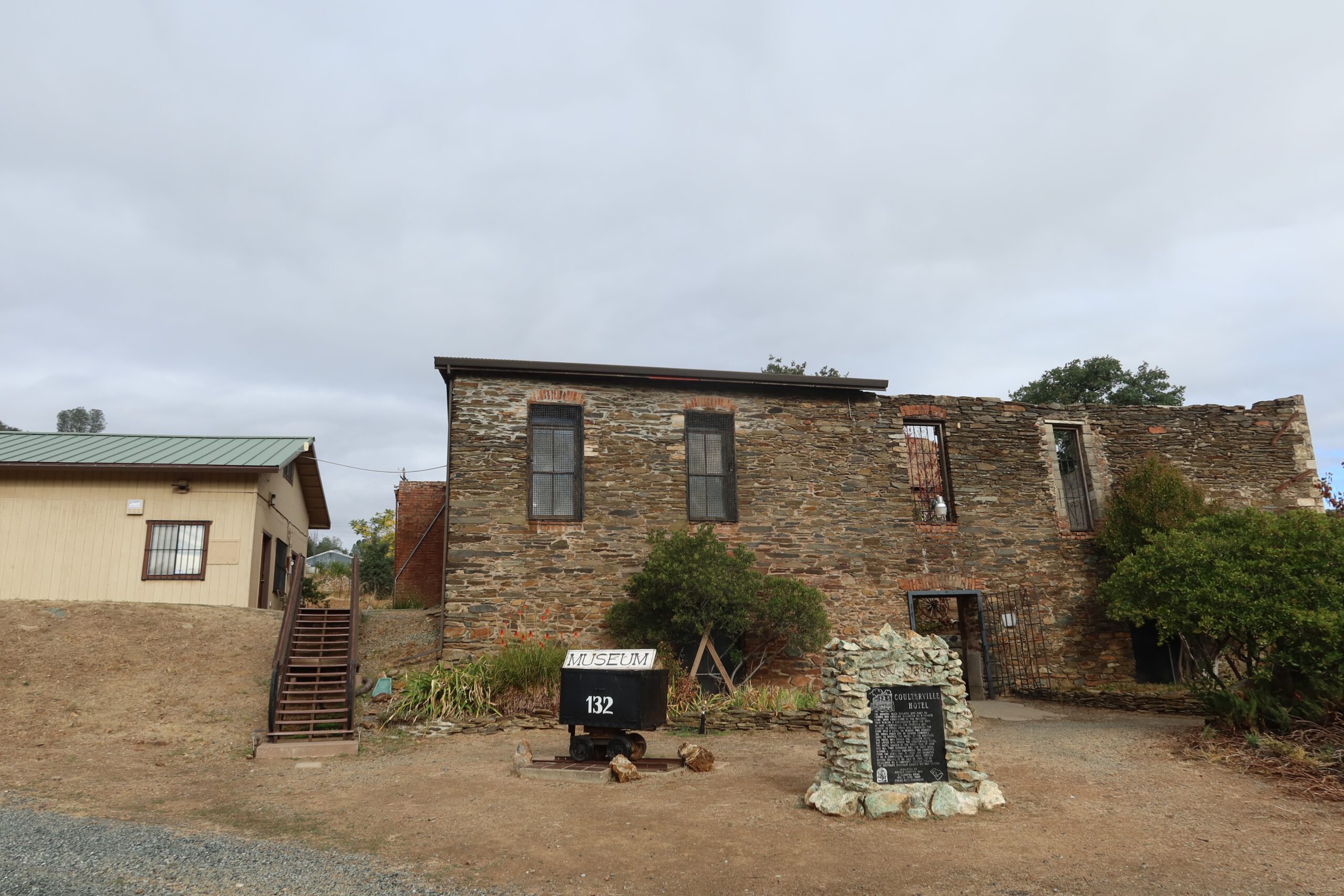Wide view of the Coulterville History Center museum building in Coulterville, California, showing gold rush stone architecture, museum signage, and historic markers along CA 49 near Yosemite foothills