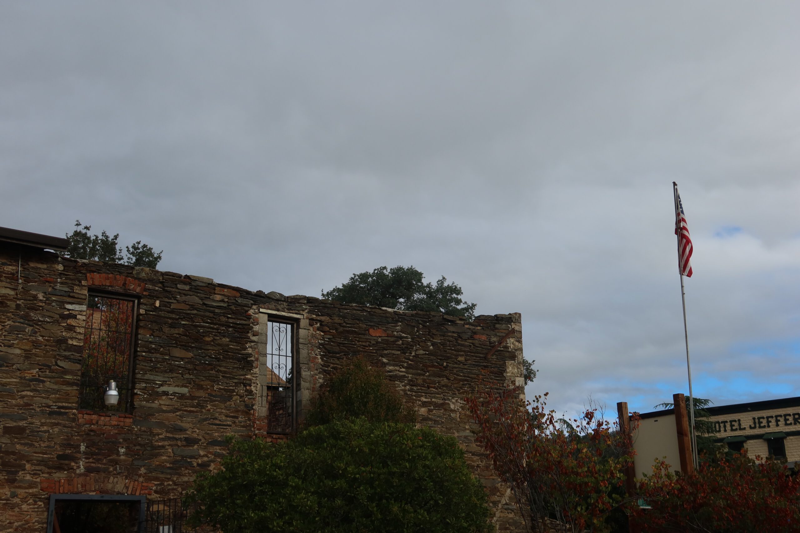 Historic stone ruins at the Coulterville History Center in Coulterville, California, featuring original gold rush era walls, iron window bars, and an American flag along CA 49 in Northern Mariposa County