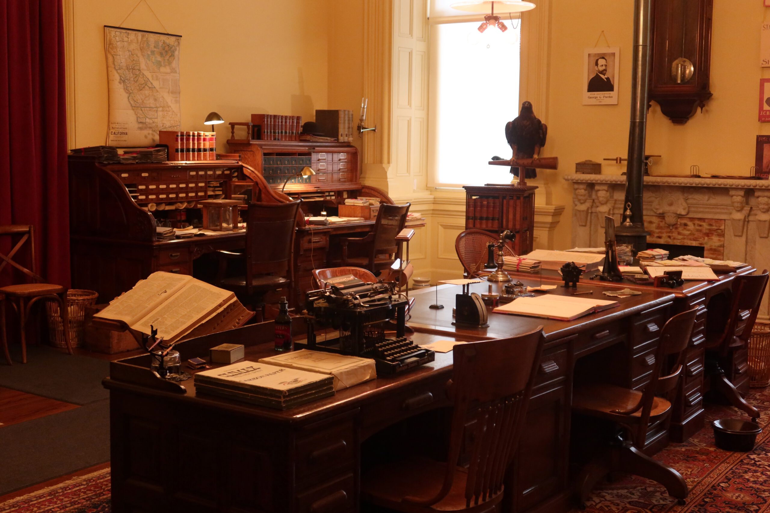 Restored historic government office inside the California State Capitol Museum, featuring wooden desks, filing cabinets, typewriters, books, maps, and period furnishings from early California state administration.