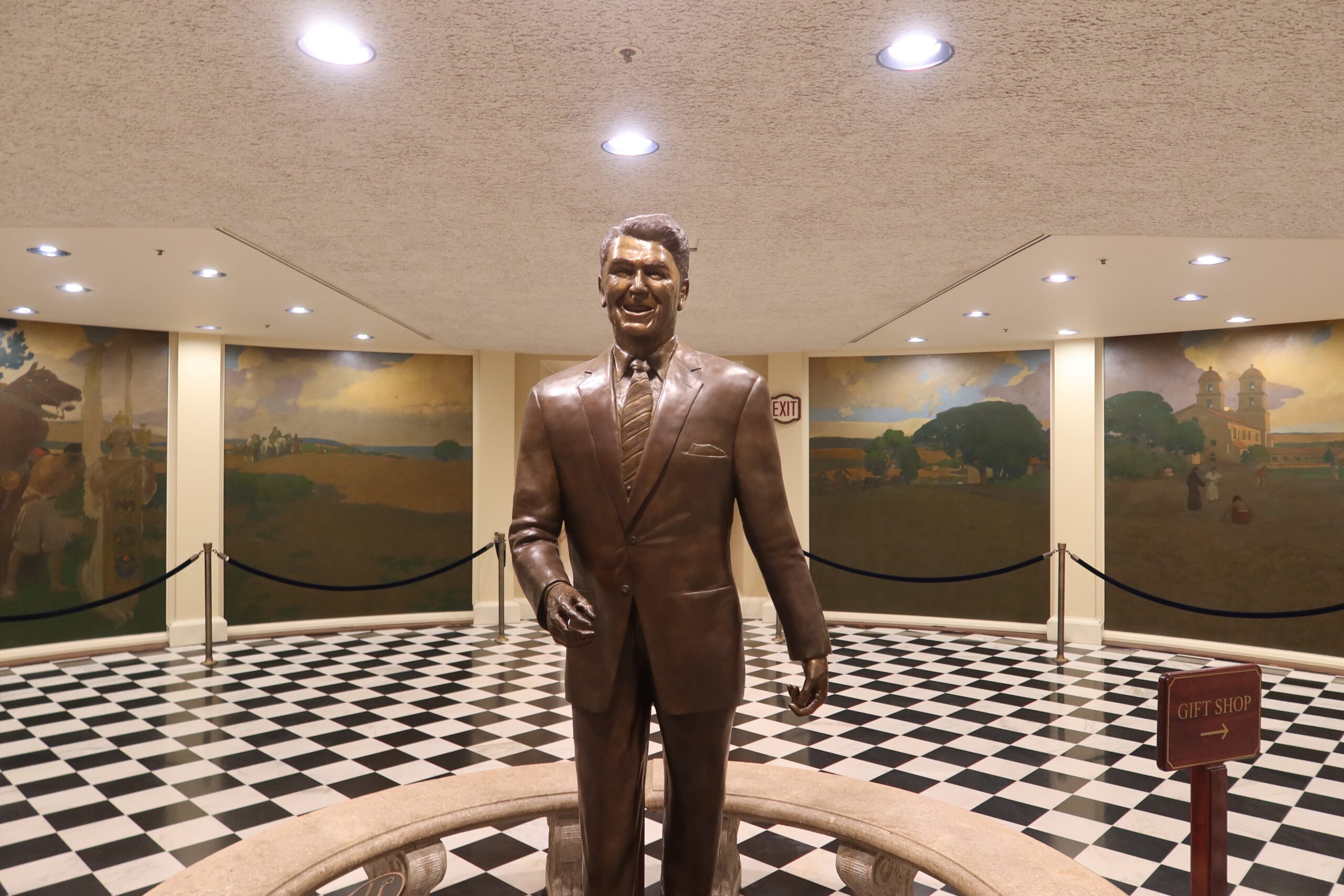 Statue of Ronald Reagan inside the California State Capitol Museum, standing in the central hall on a black and white marble floor, surrounded by historic murals and museum displays.
