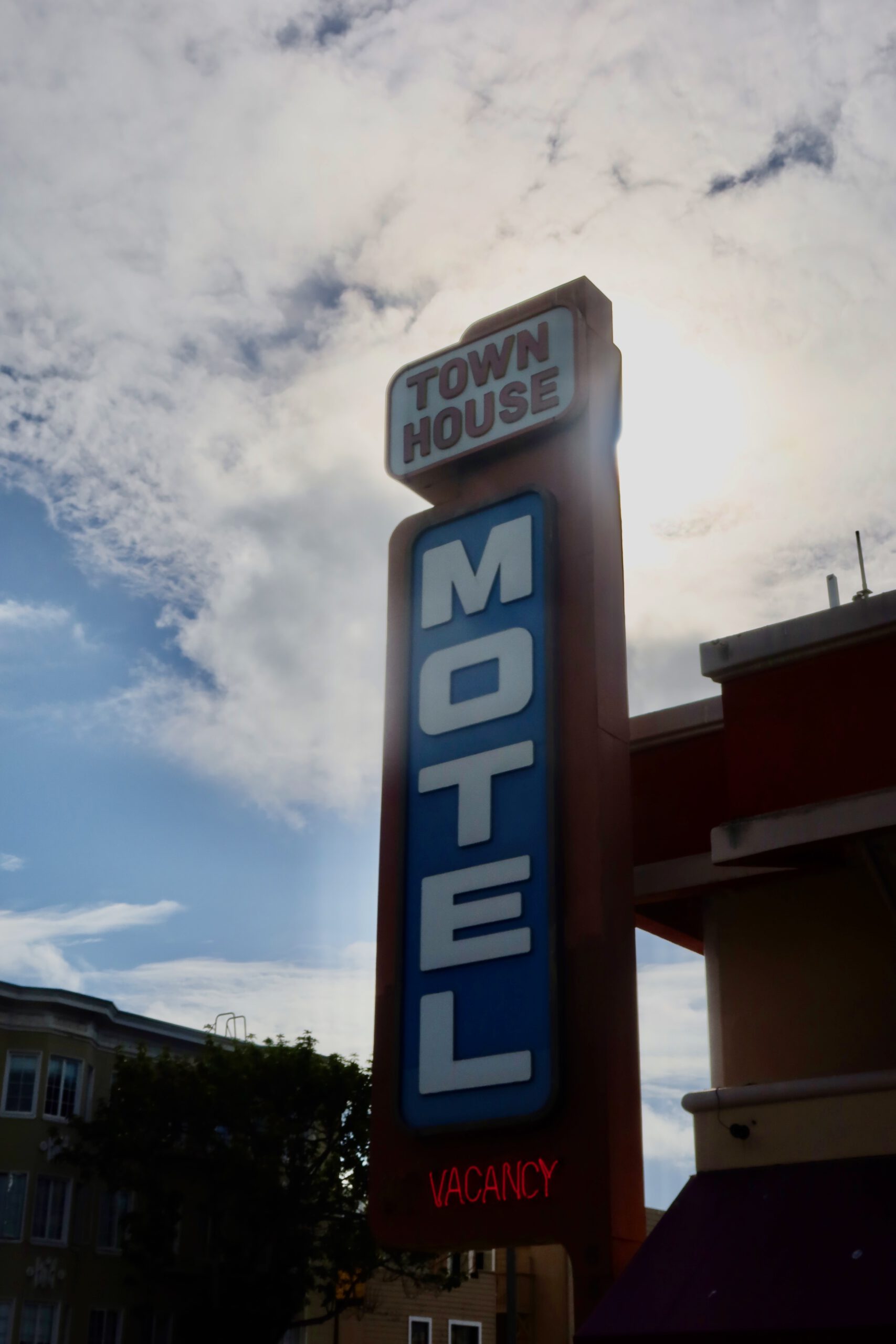 Retro Town House Motel sign in San Francisco with vertical blue ‘MOTEL’ lettering and illuminated vacancy sign against a cloudy California sky