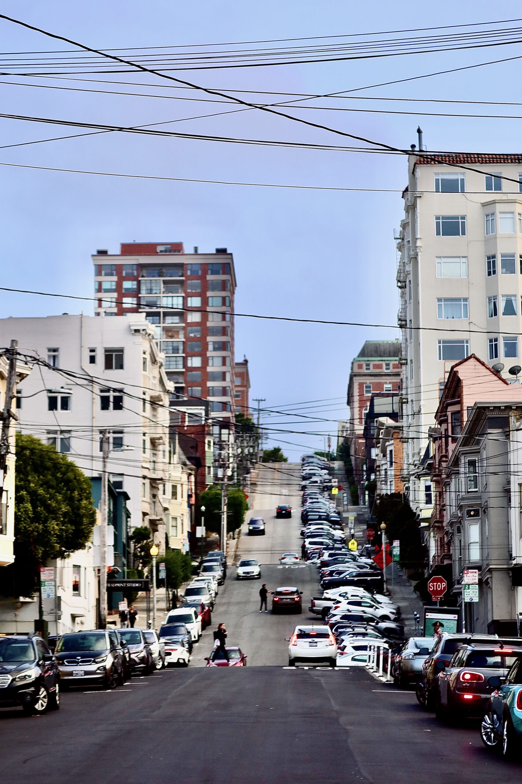 Steep residential street in San Francisco with parked cars, overhead power lines, and classic urban architecture on a clear day
