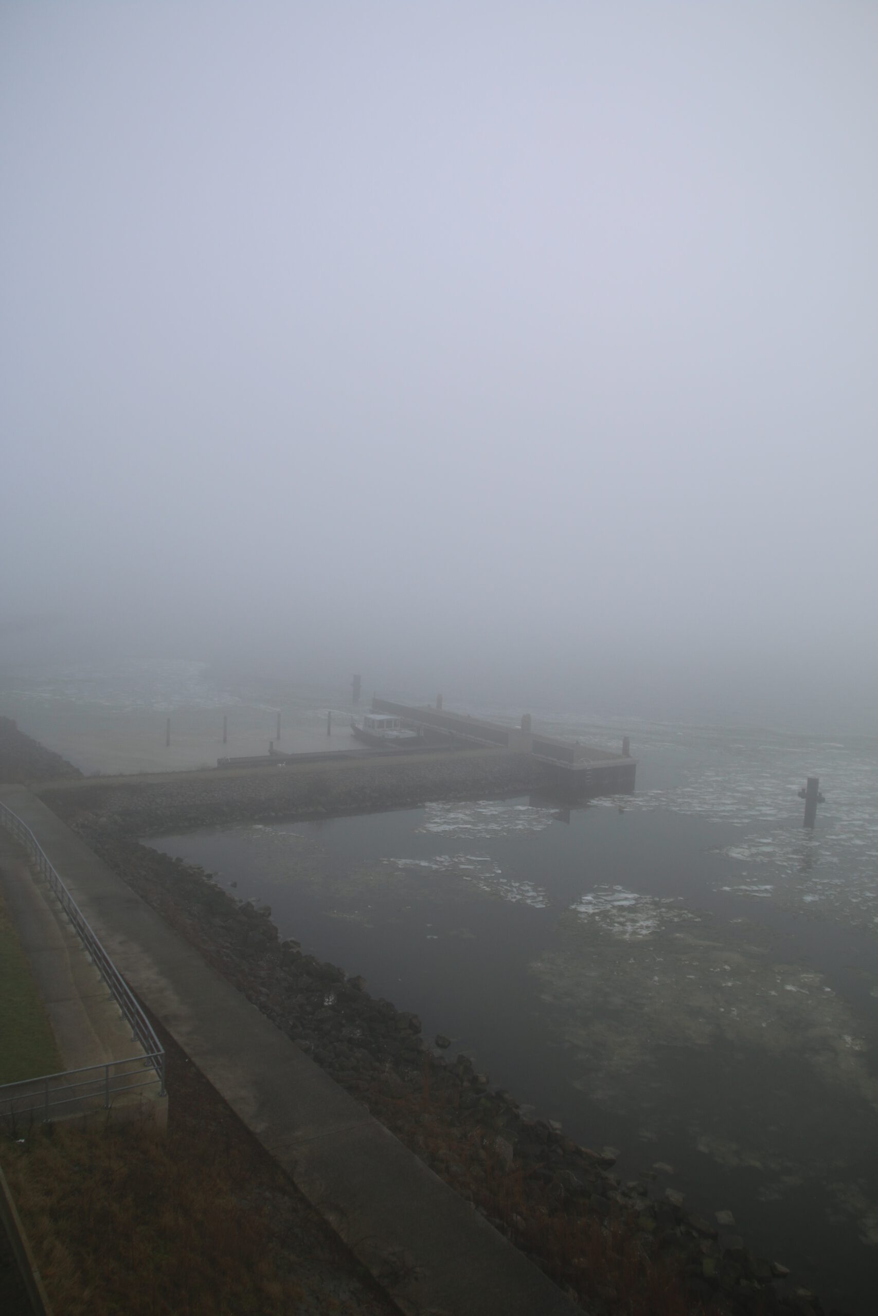 Walking Kornwerderzand near the Afsluitdijk with foggy view over water, harbor structure and quiet winter landscape