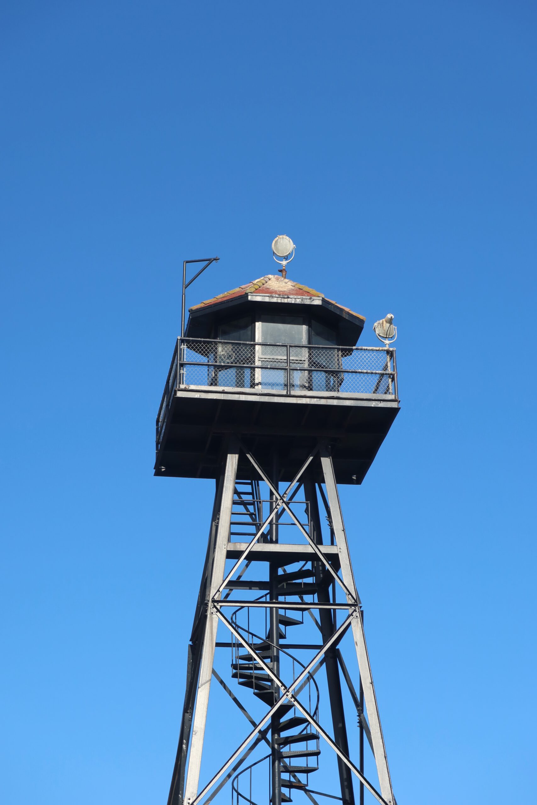 Historic guard tower on Alcatraz Island with spiral staircase and lookout platform against a clear blue sky