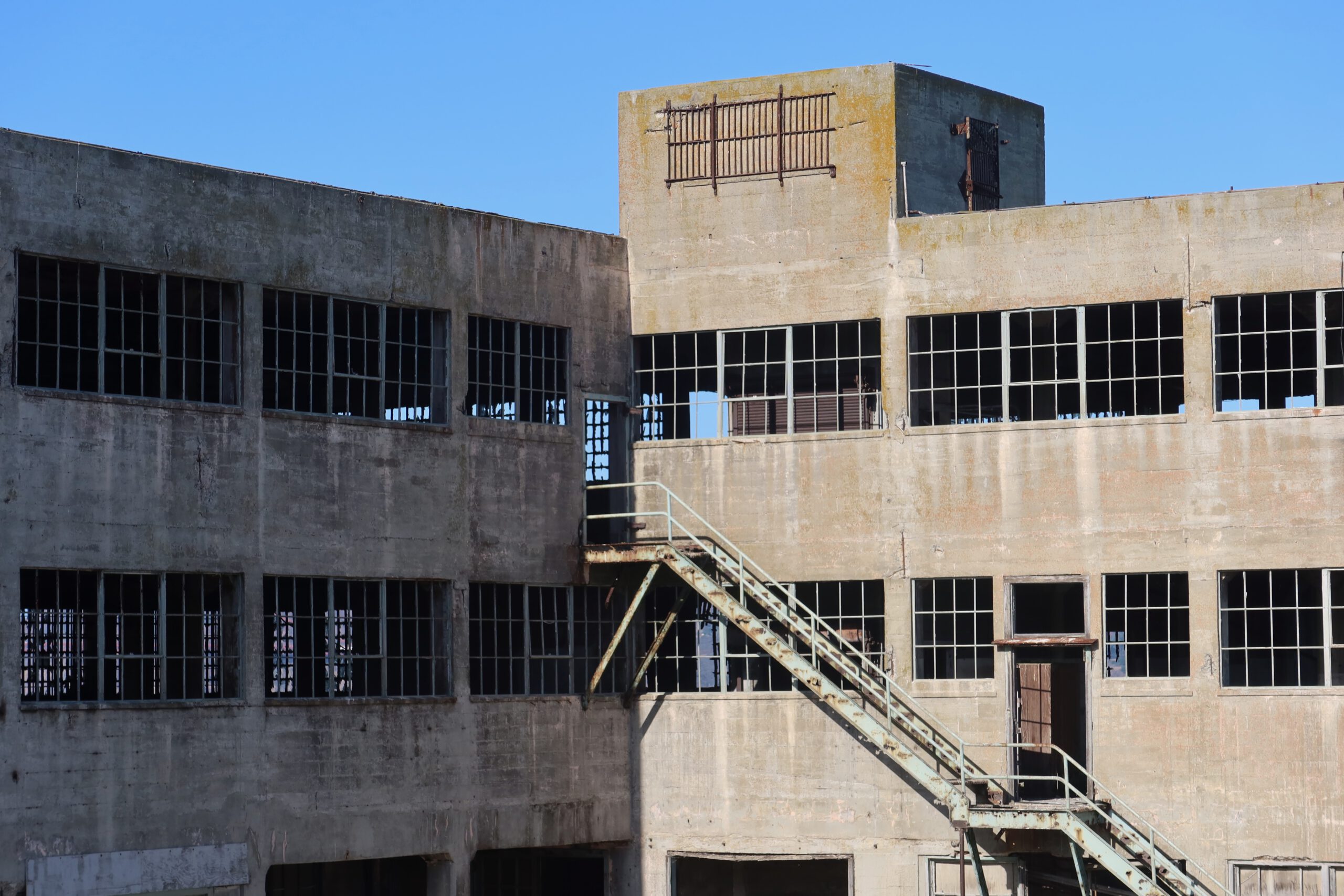 Abandoned Alcatraz Island building exterior with broken windows, exterior metal staircase, and weathered concrete walls
