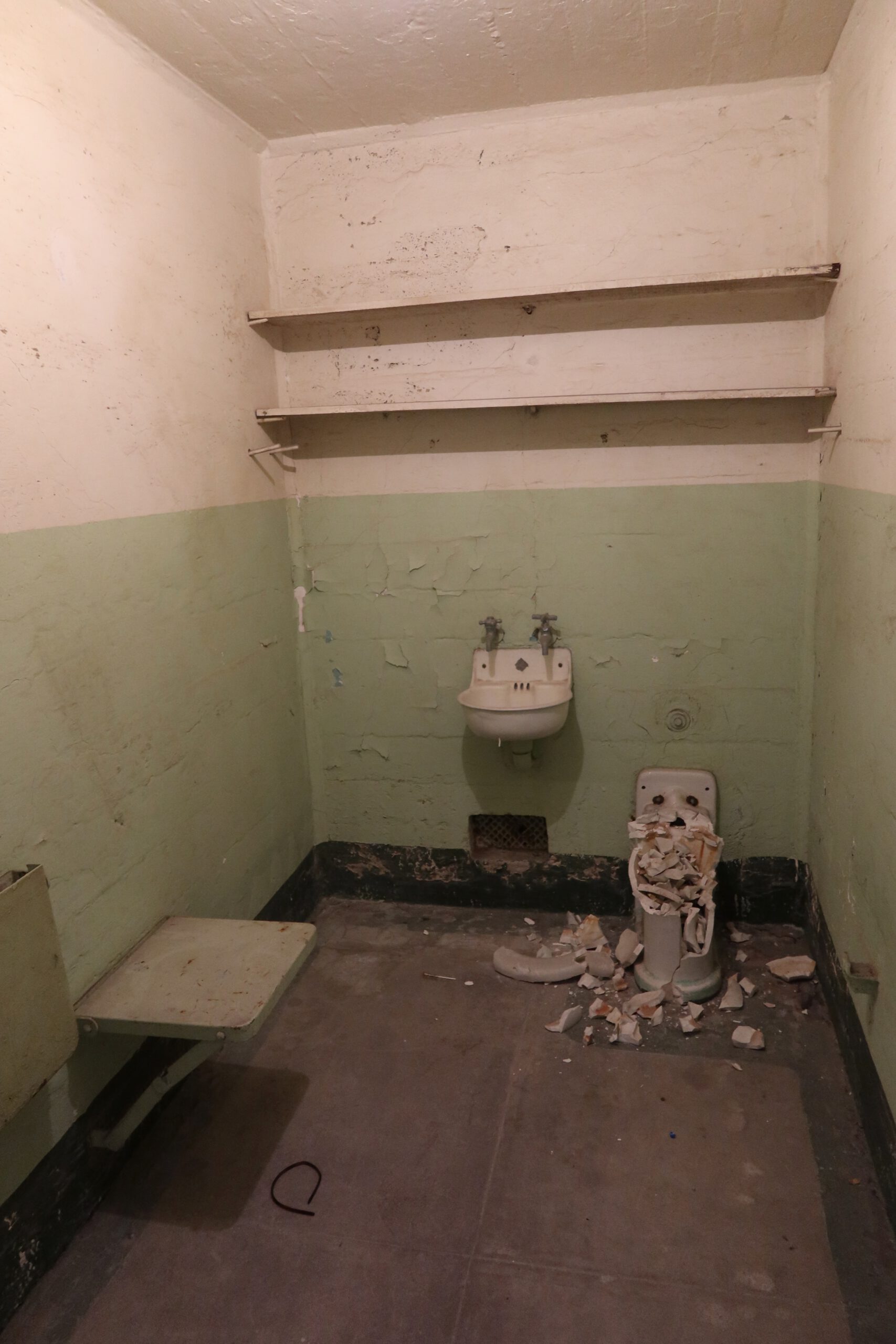 Abandoned prison cell on Alcatraz Island with broken toilet, damaged walls and exposed concrete showing decay inside the Cell House