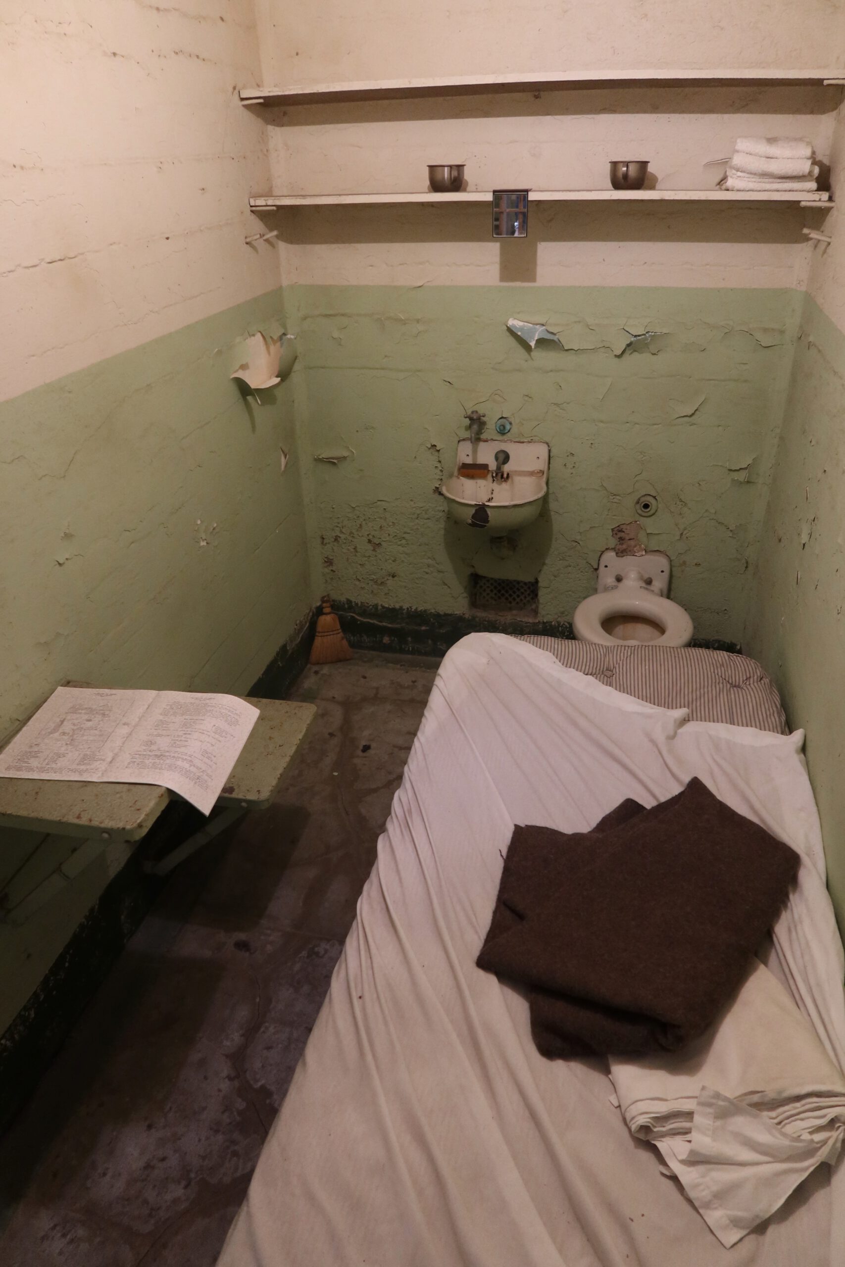 Original prison cell on Alcatraz Island with narrow bed, metal sink, toilet and peeling green walls inside the Cell House