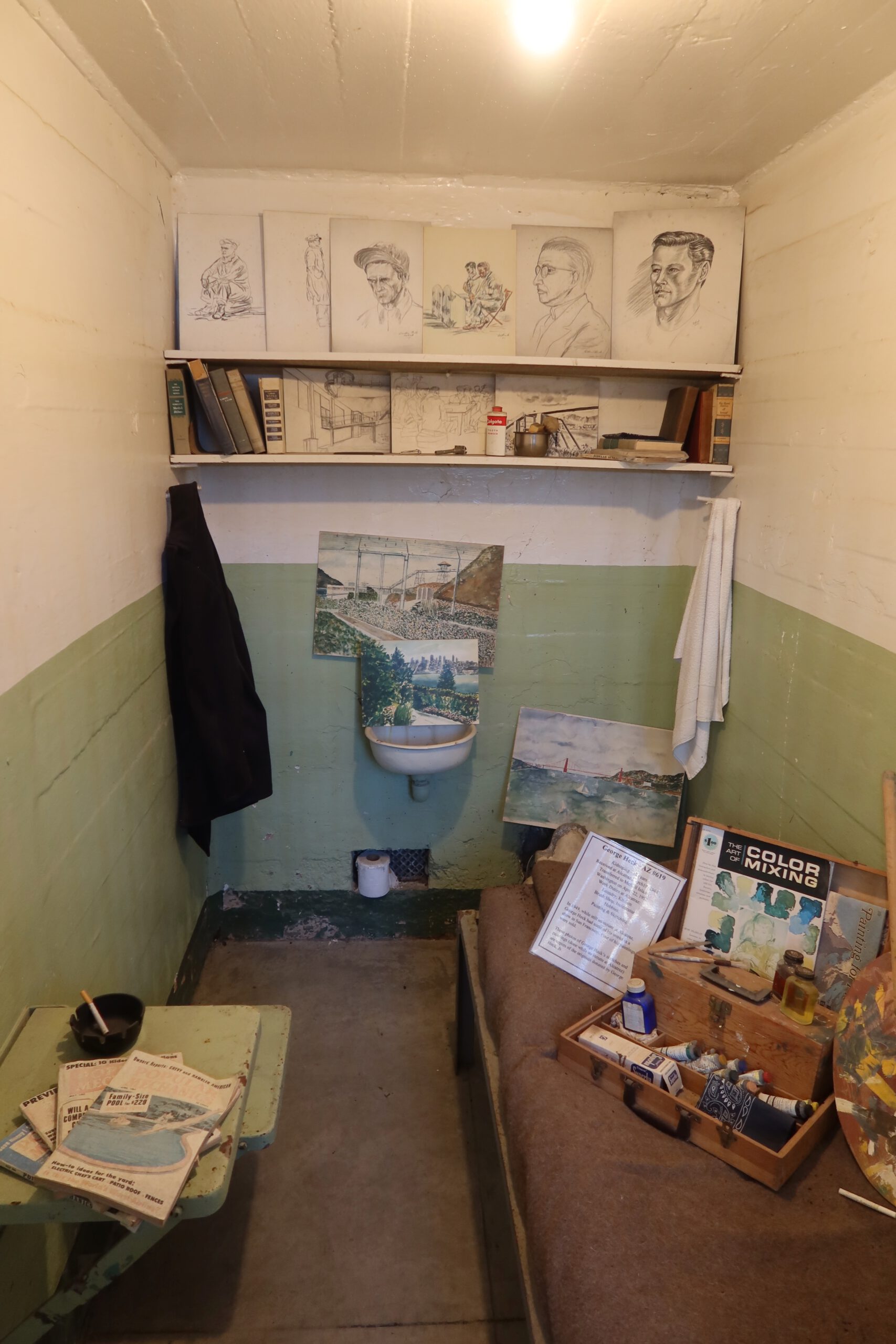 Former inmate art cell on Alcatraz Island showing drawings, paintings, books and personal items inside a restored prison cell