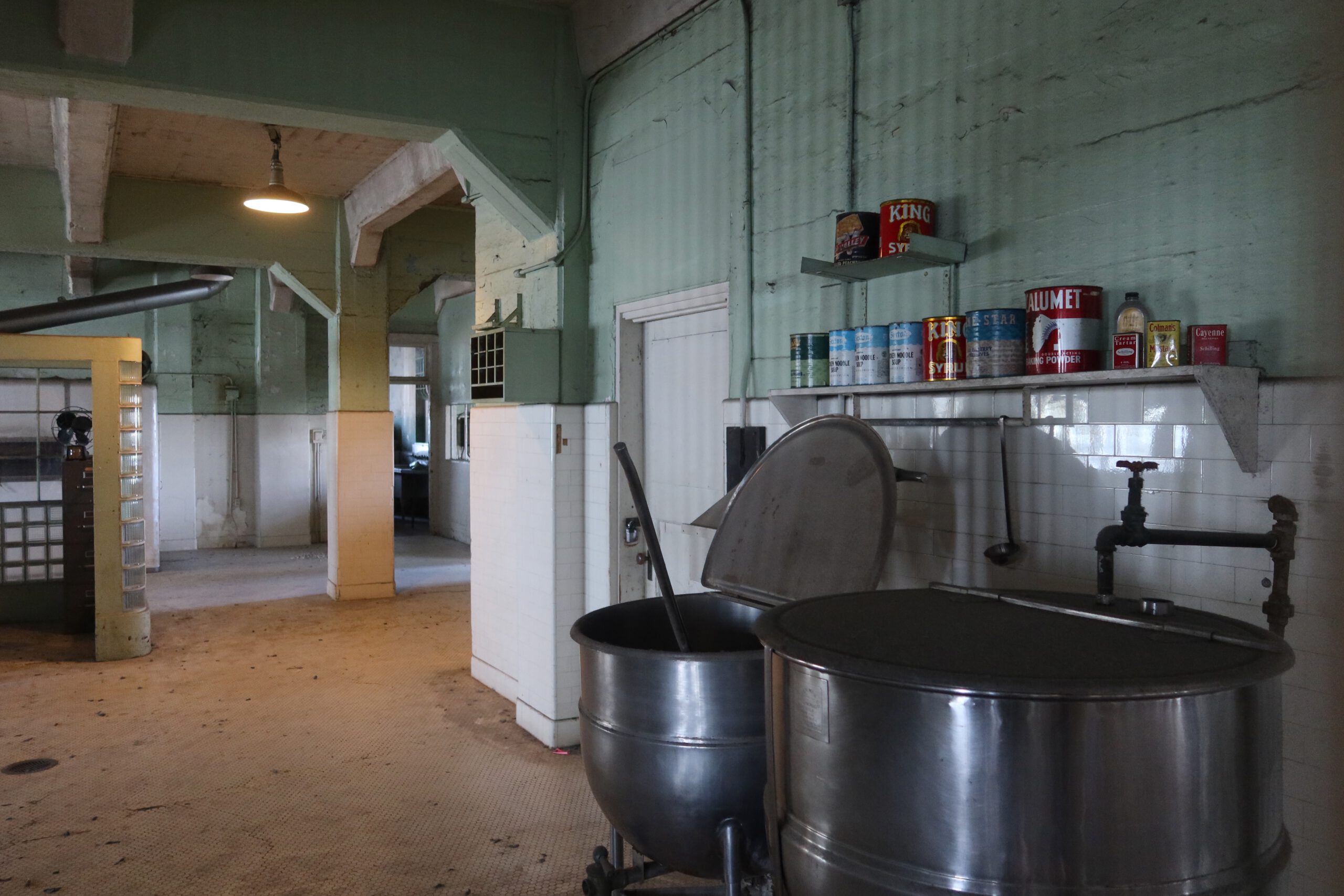 Historic prison kitchen on Alcatraz Island with large metal cooking kettles, original shelves and food preparation area