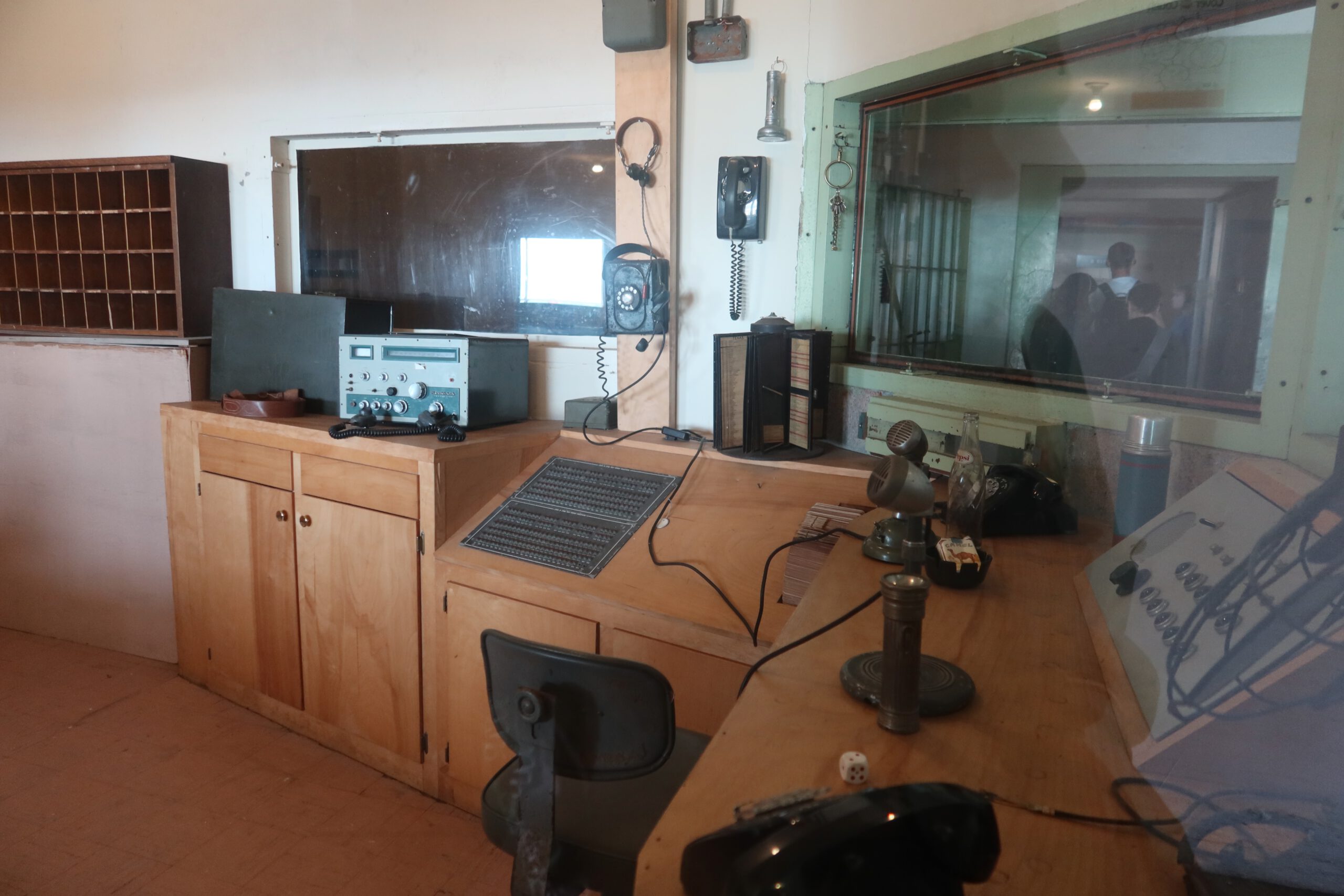 Historic Alcatraz Island control room with original communication equipment, wooden desks, microphones, telephones, and viewing windows into the prison cell blocks