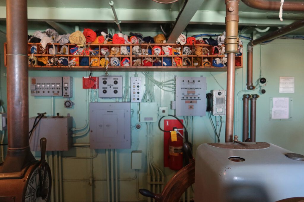 Engine control room inside the SS Jeremiah O'Brien San Francisco, featuring vintage electrical panels, fire extinguisher, piping systems, and original ship machinery from World War II.